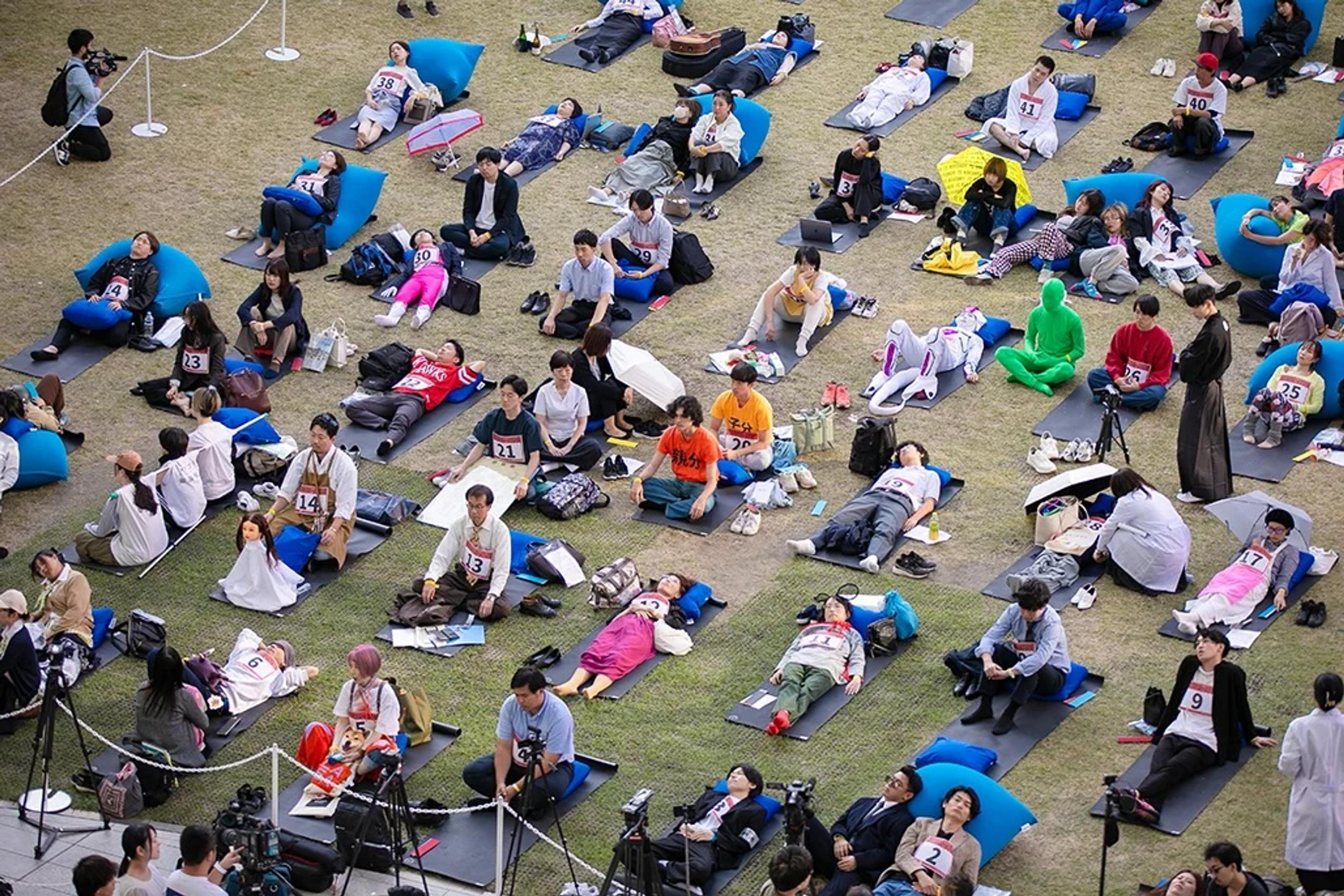 Bird's eye view of competitors lying on their backs on mats in a grassy field, staring into blank space