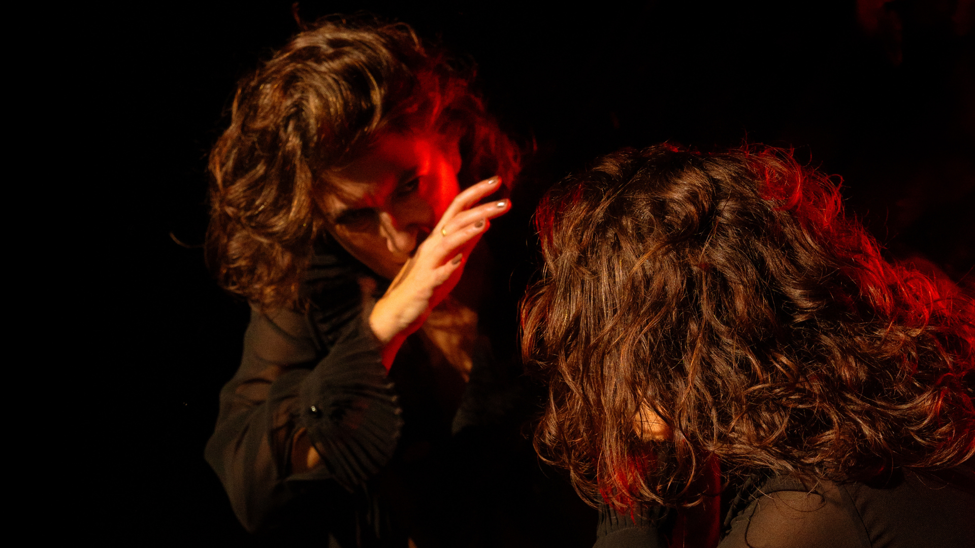 A dancer on their knees looking at themselves in the mirror with the edge of their hand covering their mouth.
