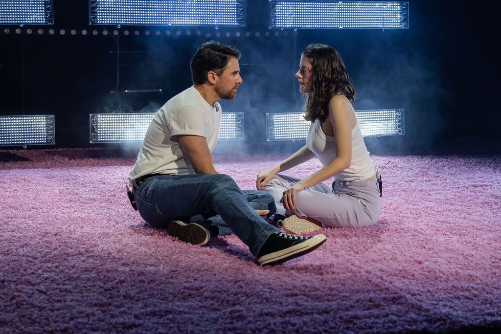 Two actors sit facing each other on a carpeted floor 