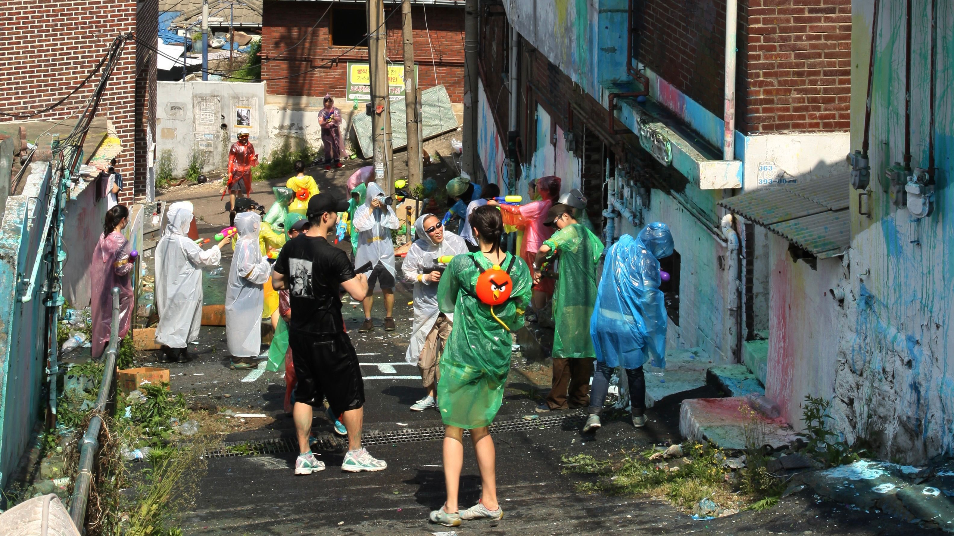 A group of people gather the street wearing plastic ponchos doing a playful urban activity