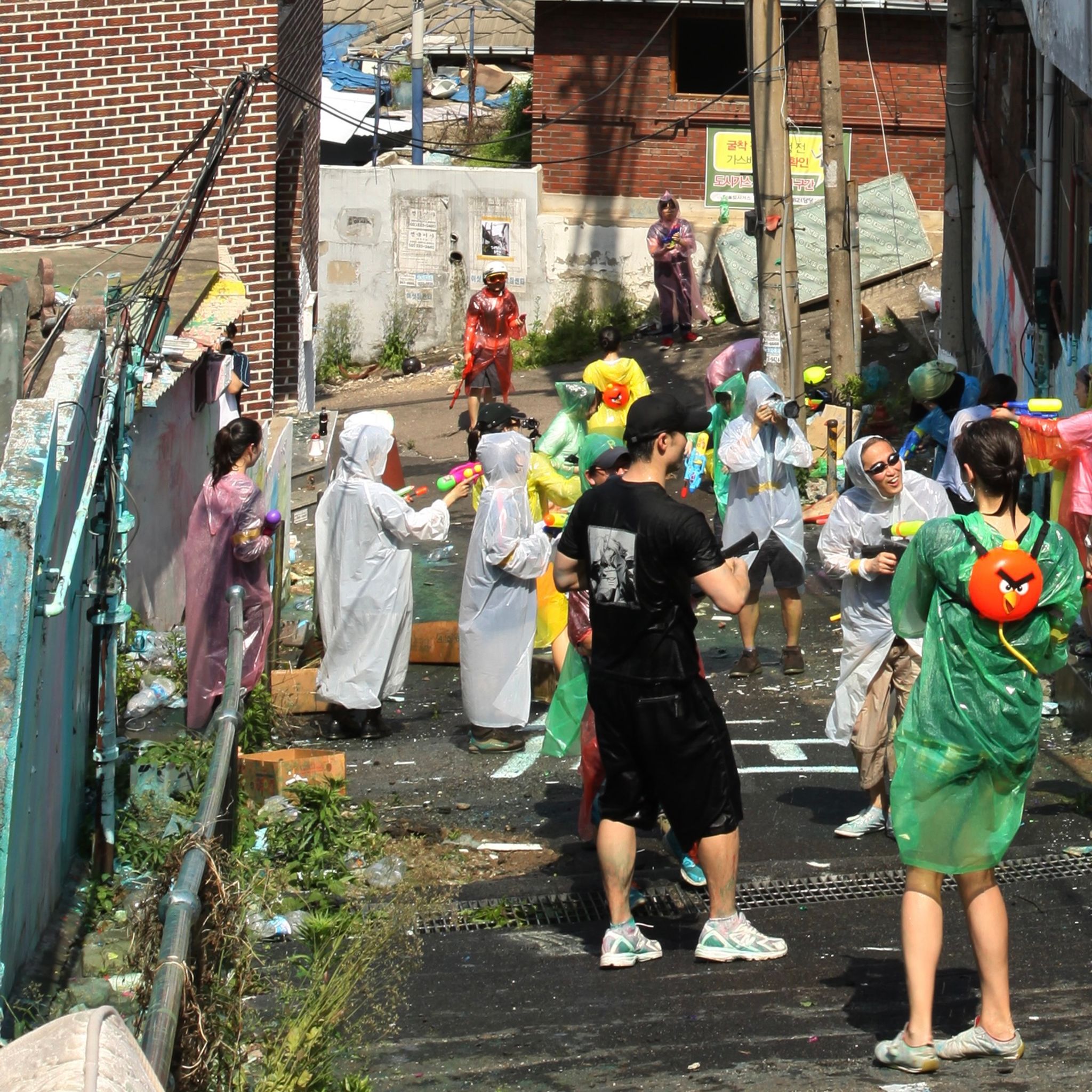 A group of people gather the street wearing plastic ponchos doing a playful urban activity