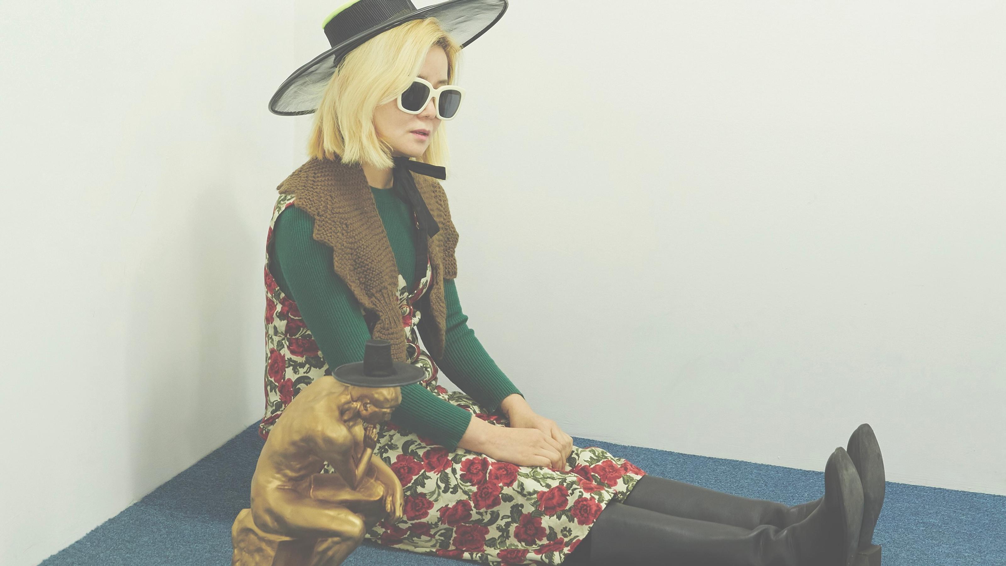 Artist Woospang sitting on the ground wearing a wide-brimmed hat and sunglasses.