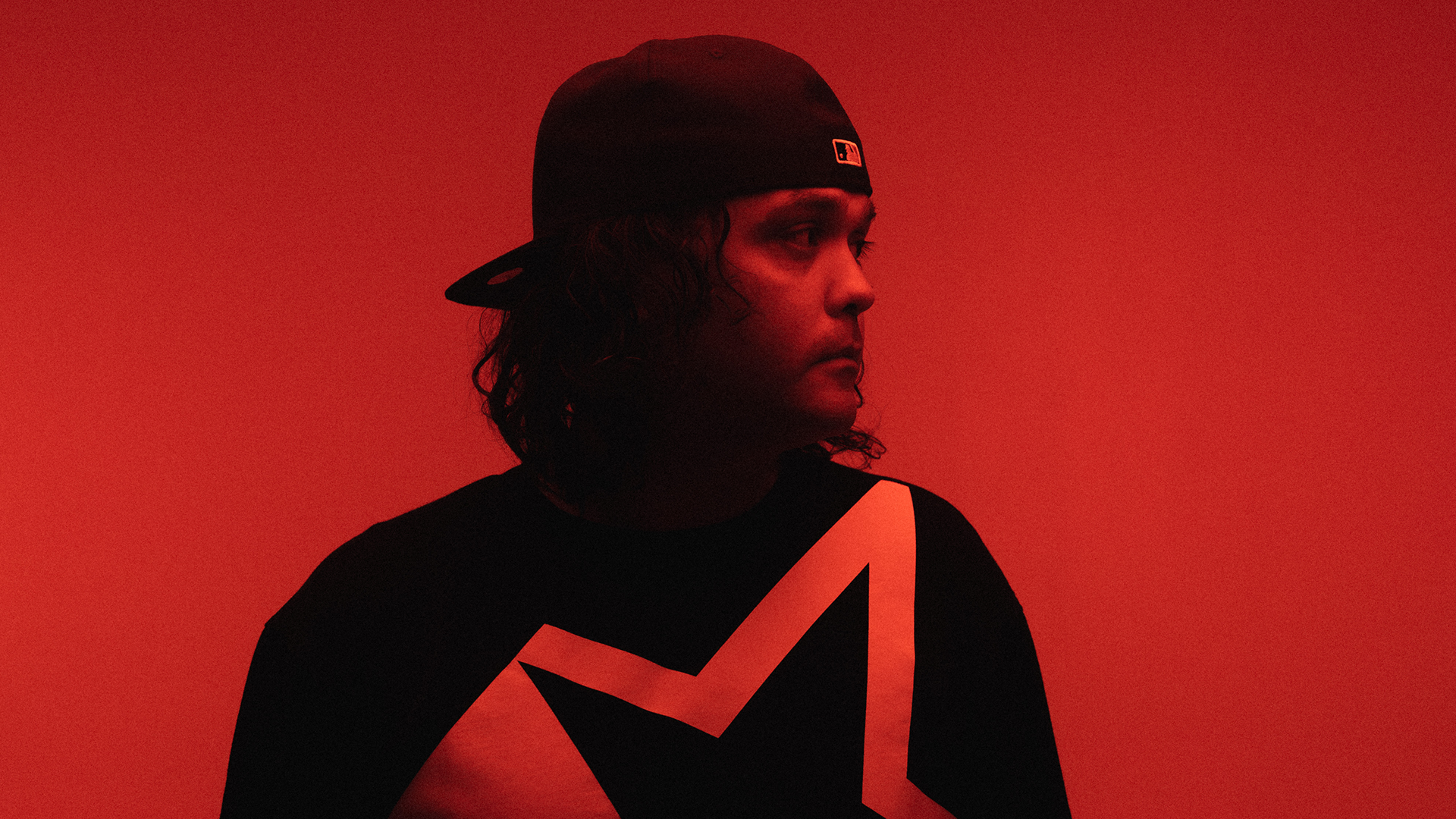 Rapper Birdz faces the camera, wearing a flat cap backwards, and looks out to the right of frame