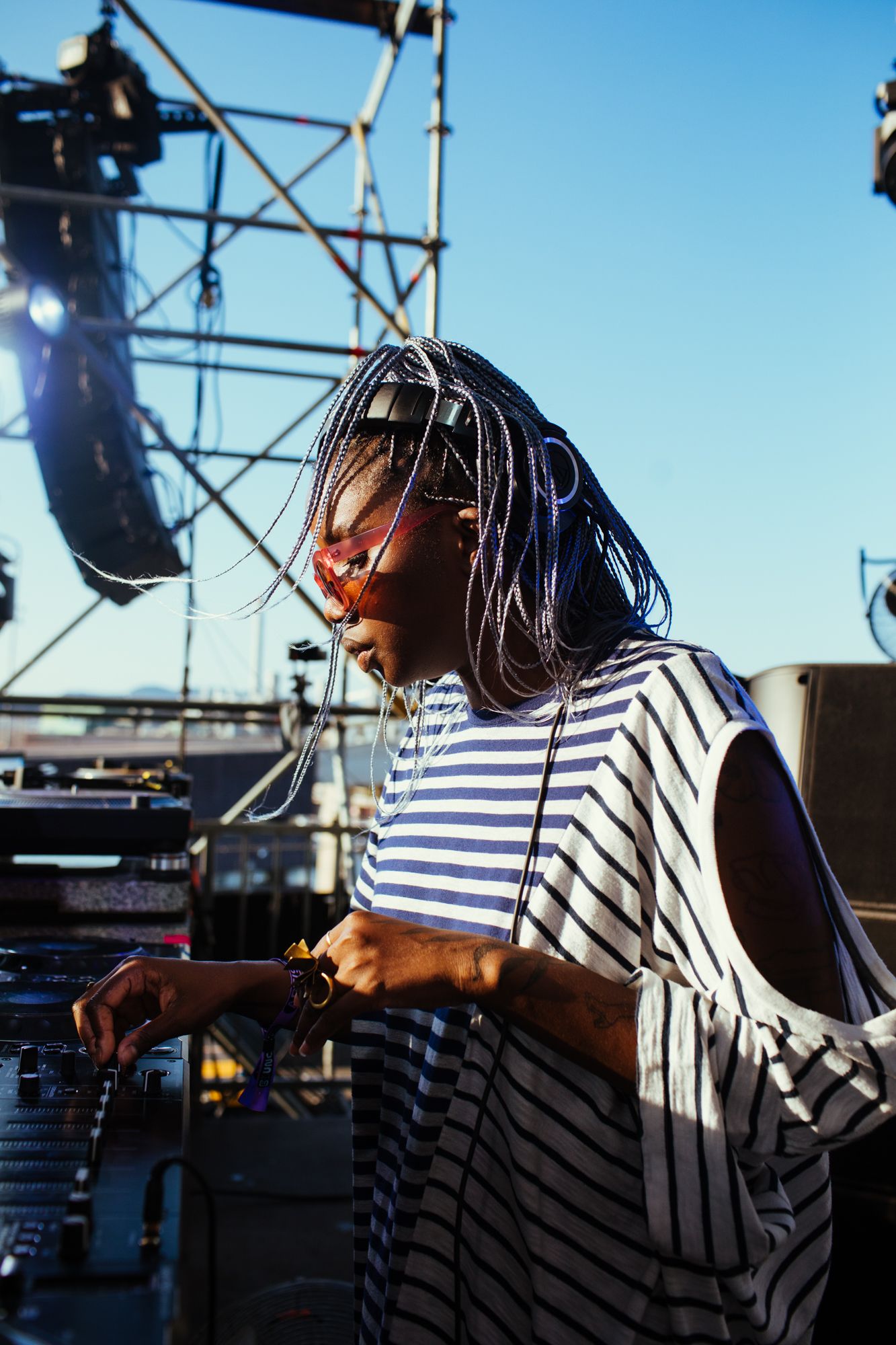 A DJ with a striped shirt and braided hair performs at an outdoor event.