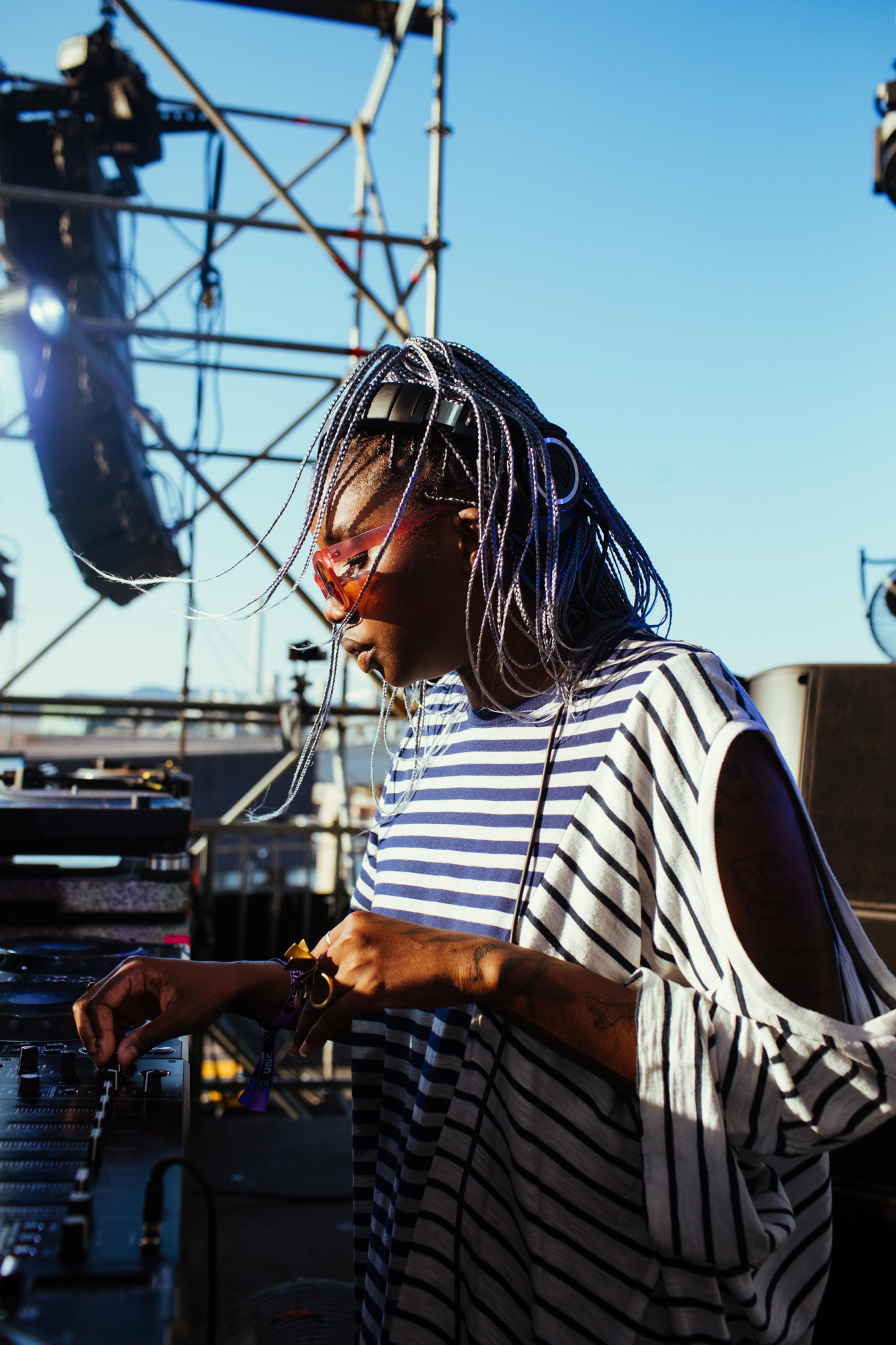 A DJ with a striped shirt and braided hair performs at an outdoor event.