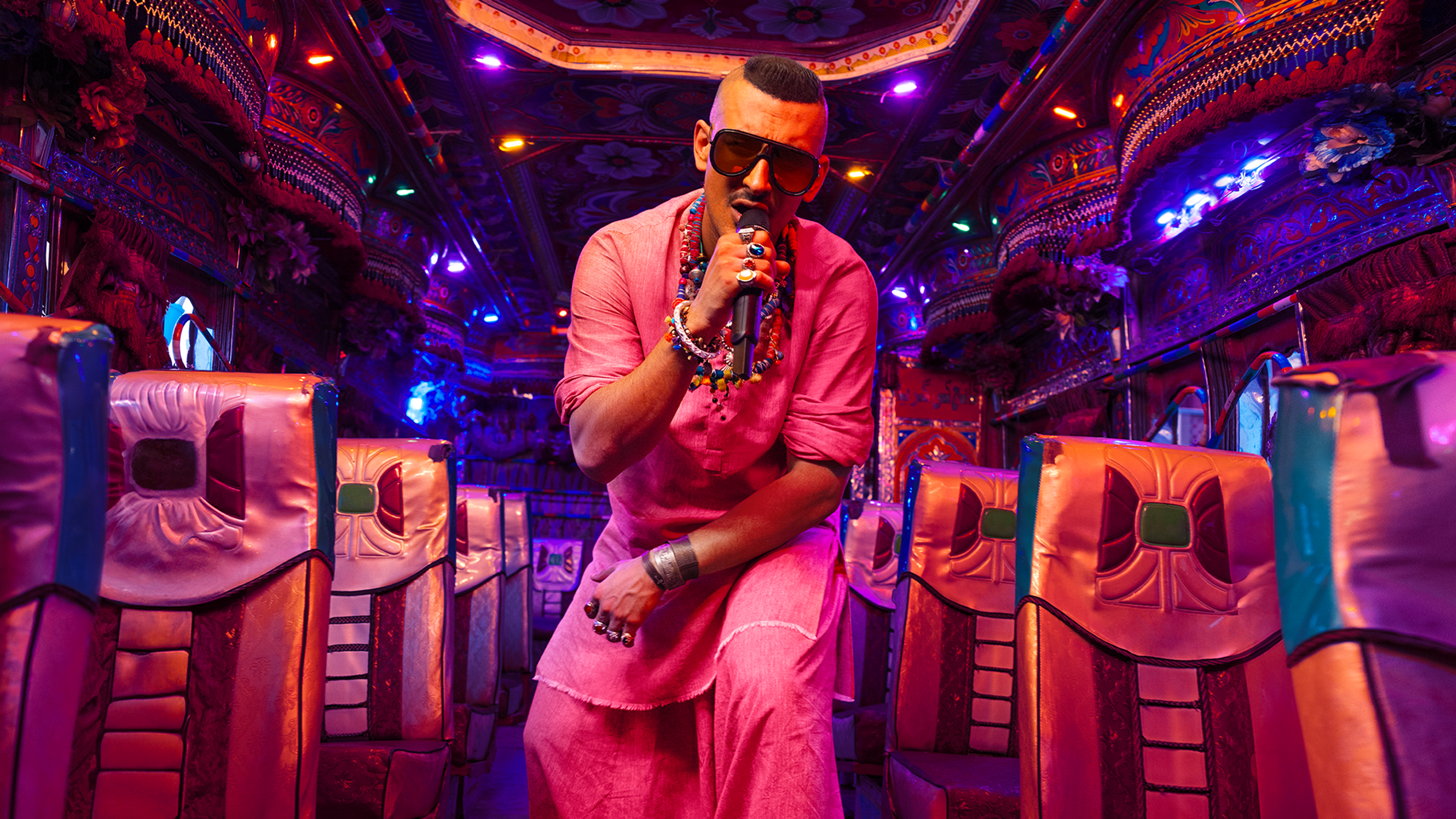 Dressed in pink, Faris Shafi performs in a multi-coloured, vibrantly lit bus.