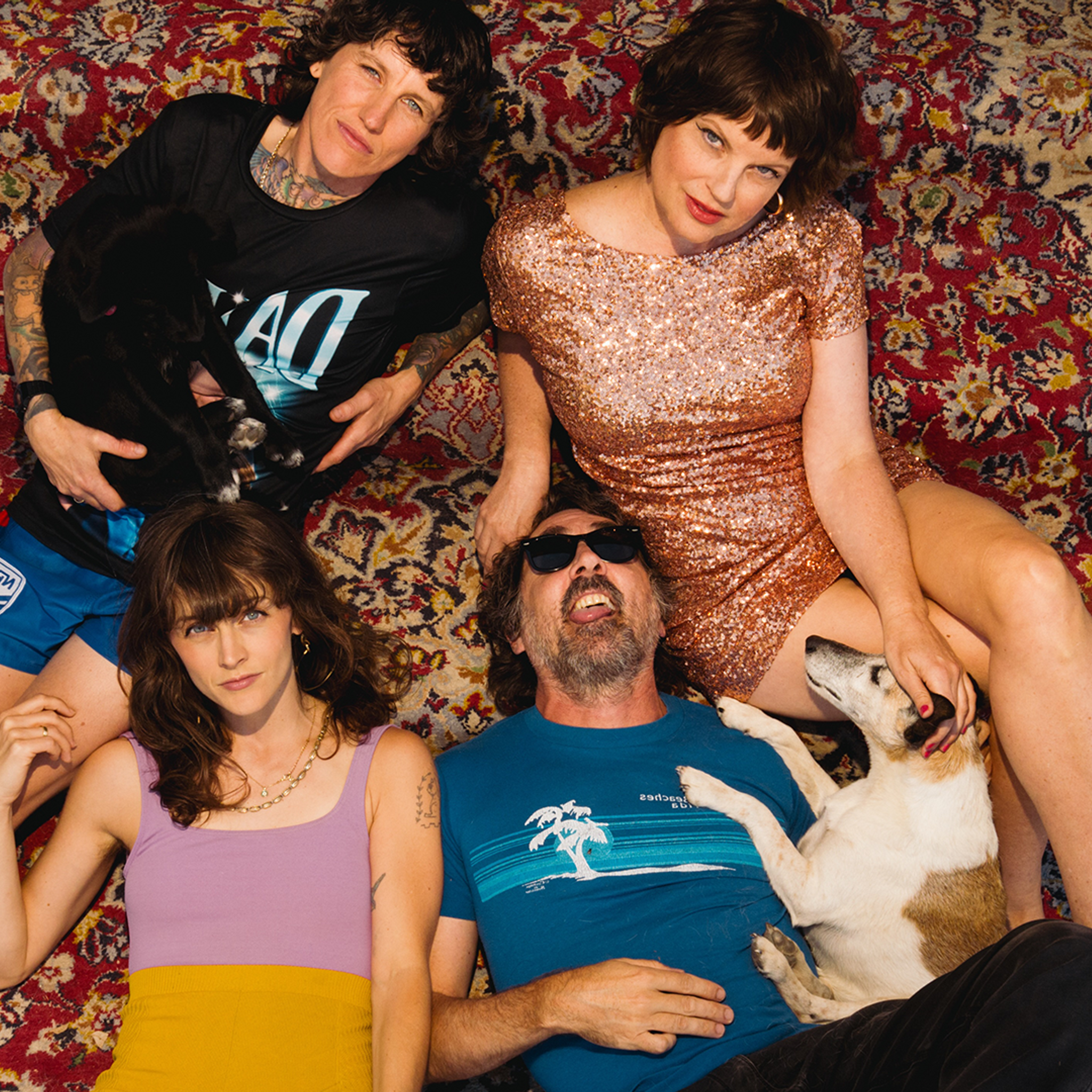 A birds eye view of four people laying back on a persian rug, looking up into the camera. A dog joins in