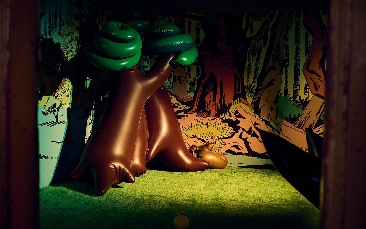 A darkened room featuring a cartoonish landscape filled with inflatable trees, flies and poops.