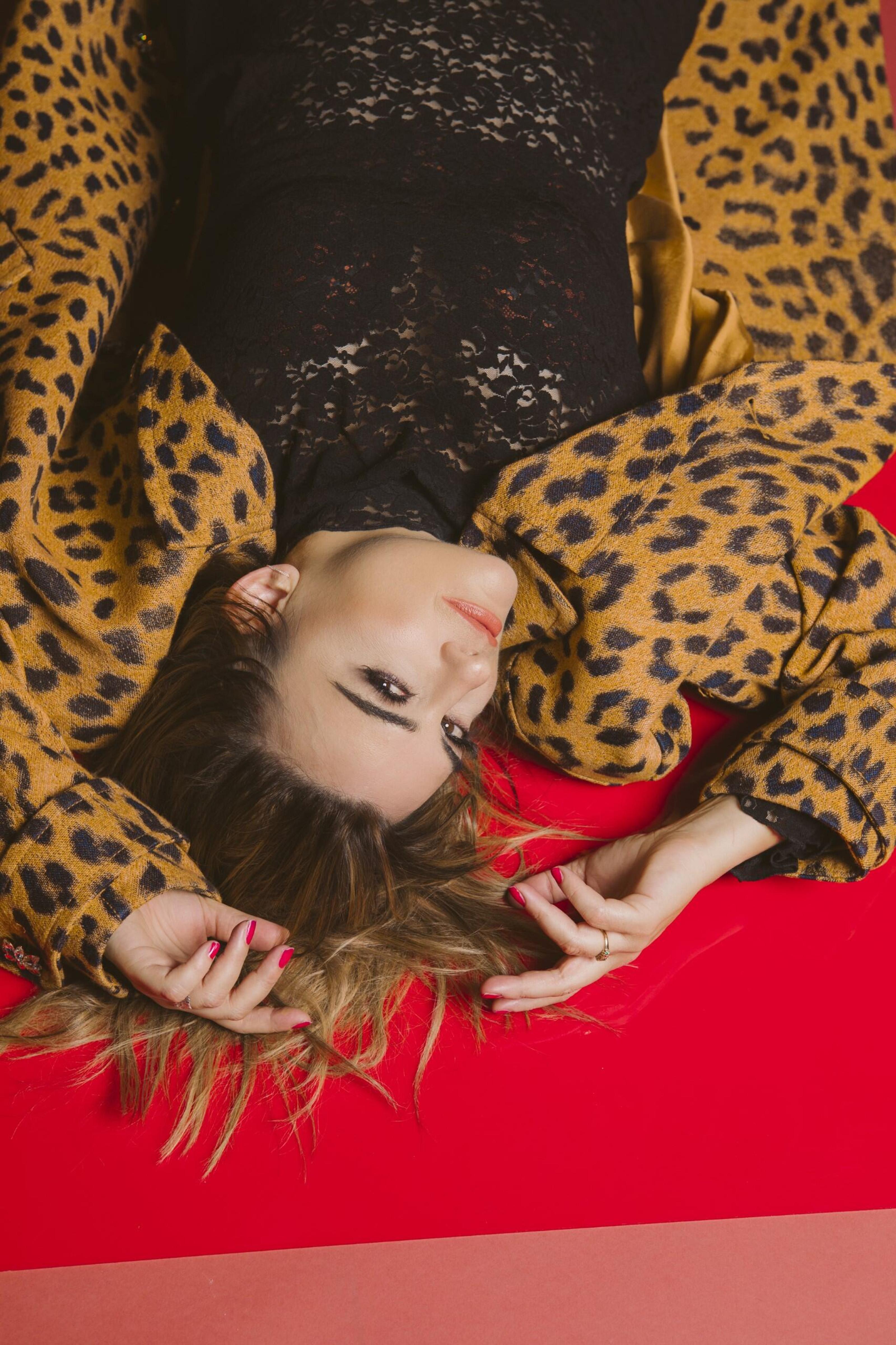 An upside down face of a woman laying on the floor, hair splayed, and wearing a leopard-print jacket