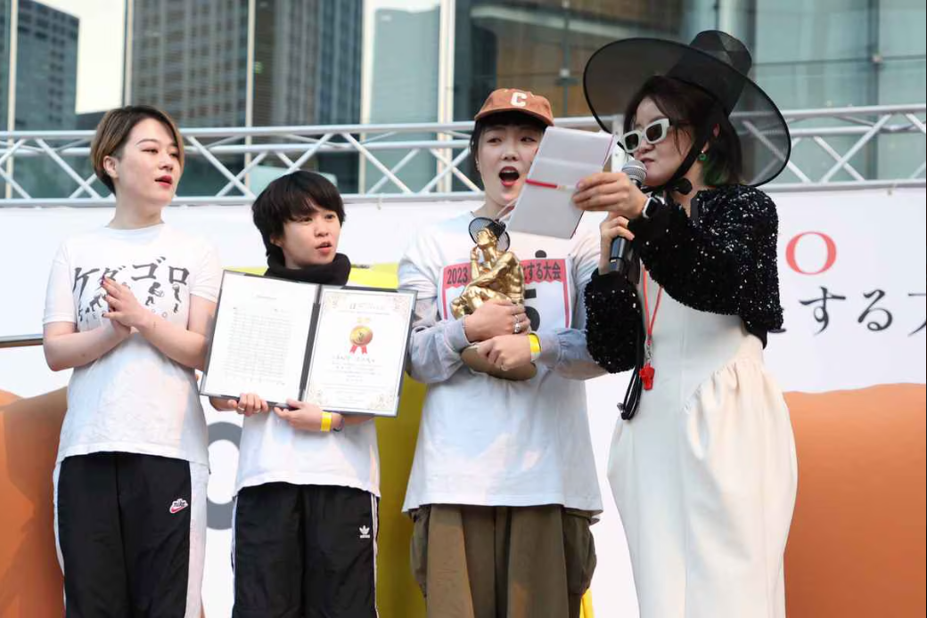 Three competitors holding certificate and trophy expressing shock, with host dressing in traditional korean hat 