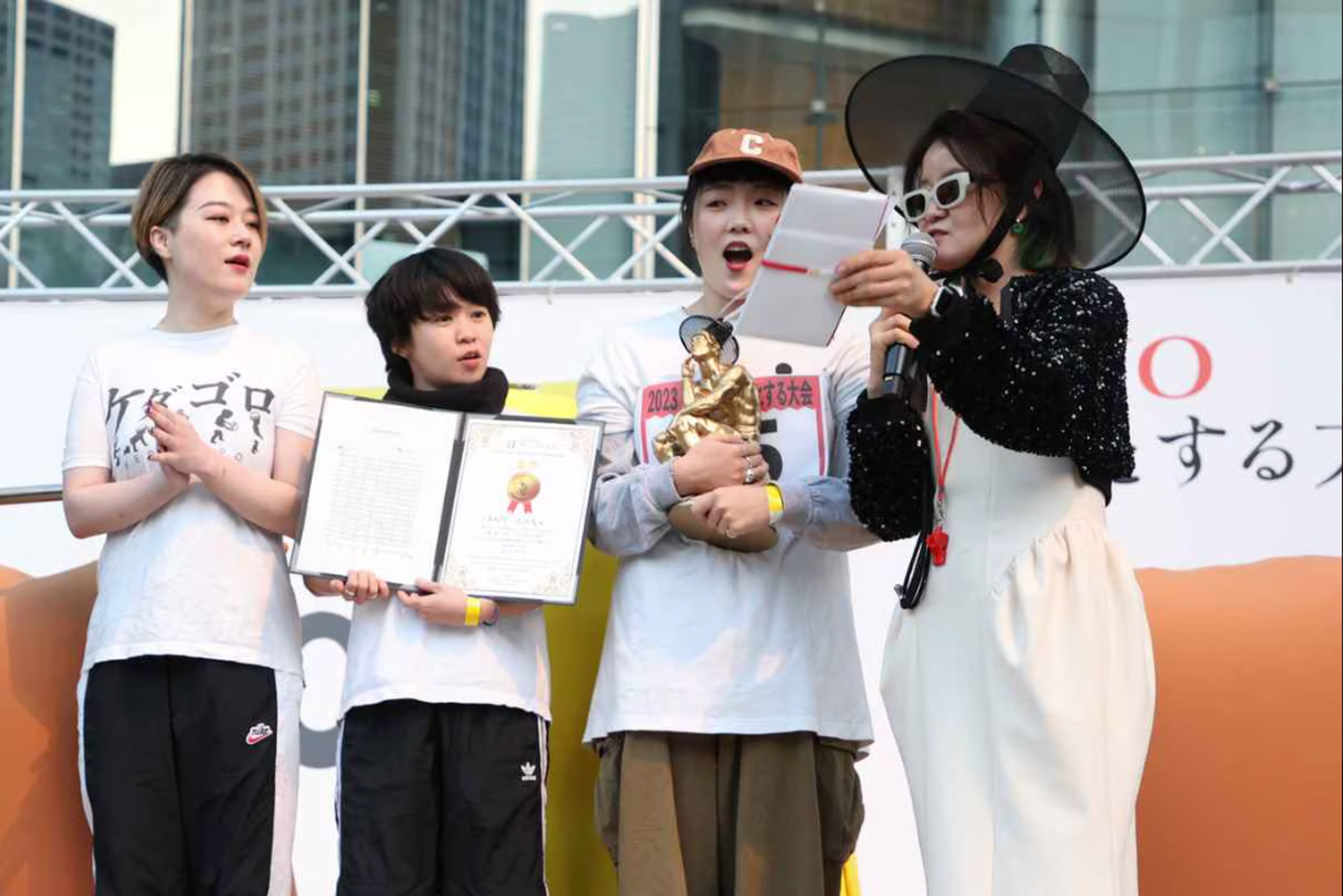 Three competitors holding certificate and trophy expressing shock, with host dressing in traditional korean hat