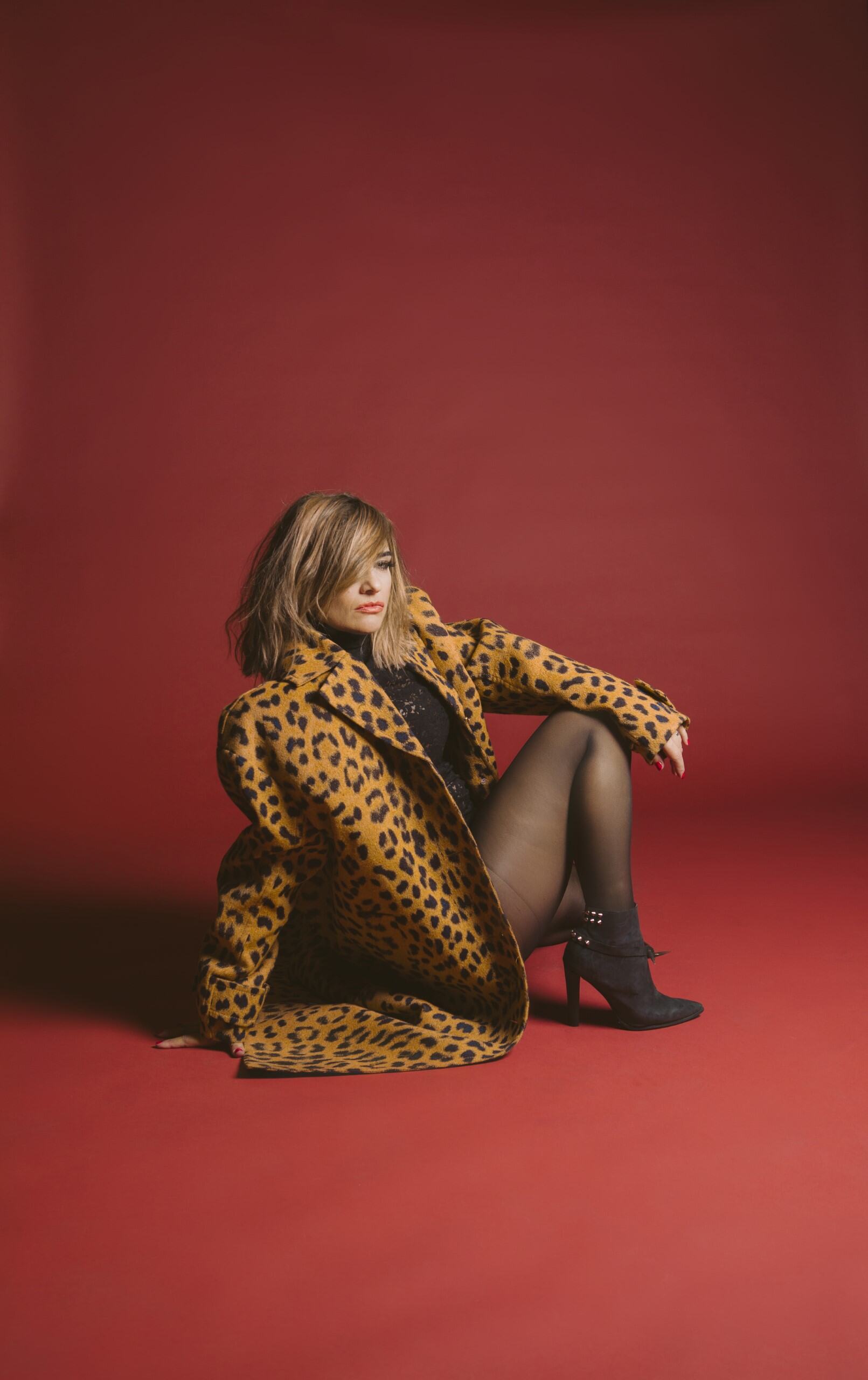  A woman wearing a leopard-print jacket and black tights and heels, sitting on the floor 