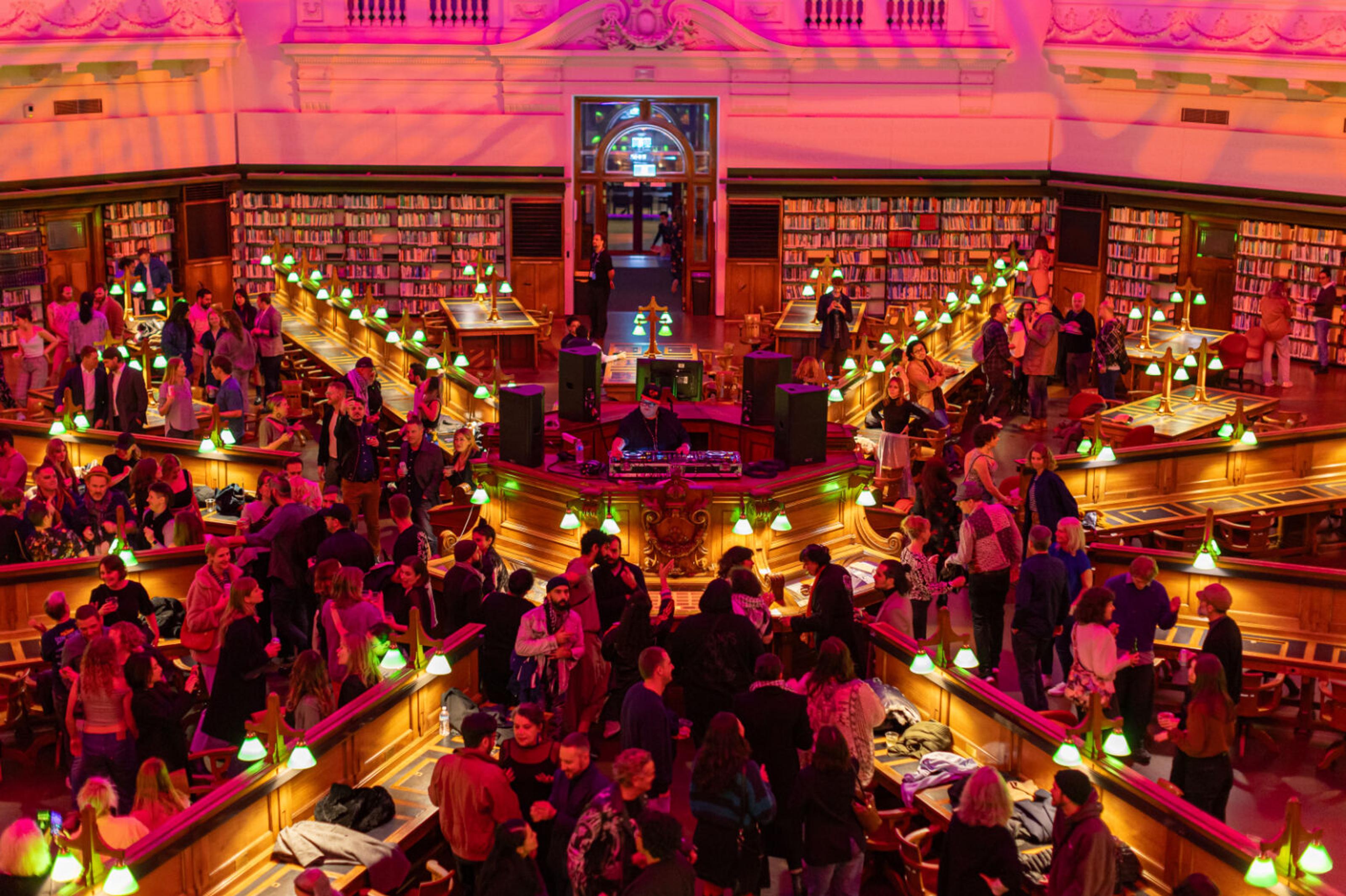 A vibrant library buzzing with energy, people engage in chatting and connecting. The music filling the space with an exciting, festival atmosphere.