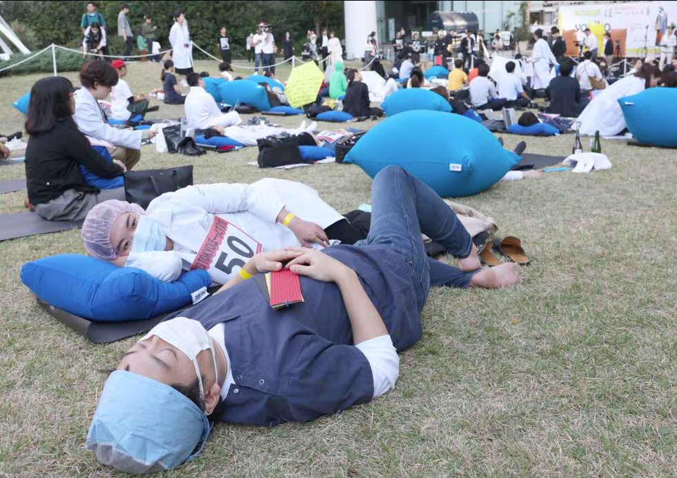 Two competitors lay down and dress in medical attires, with masks and head covers-one laying on their side, other facing upward 