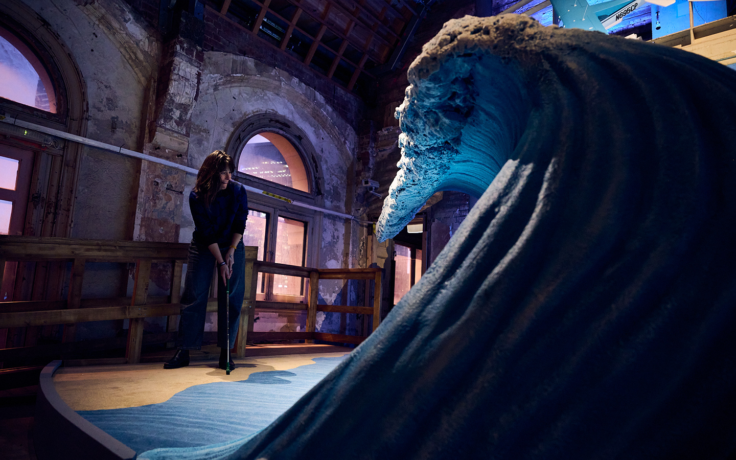 An installation view of Miranda July's mini golf hole. A person putts into a giant fibreglass wave