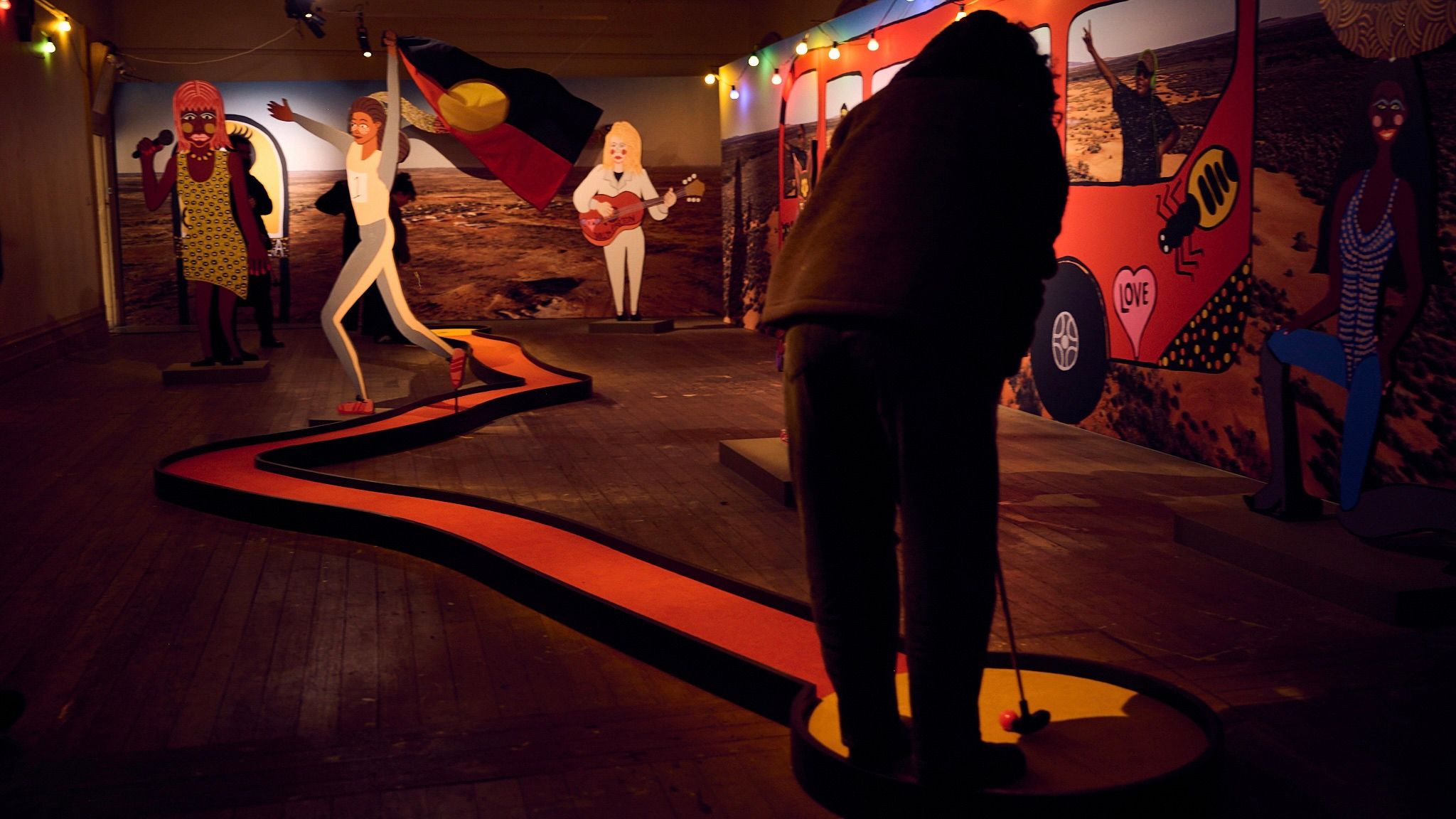 Someone lining up to putt through along a long winding carpet, themed as the Aboriginal flag