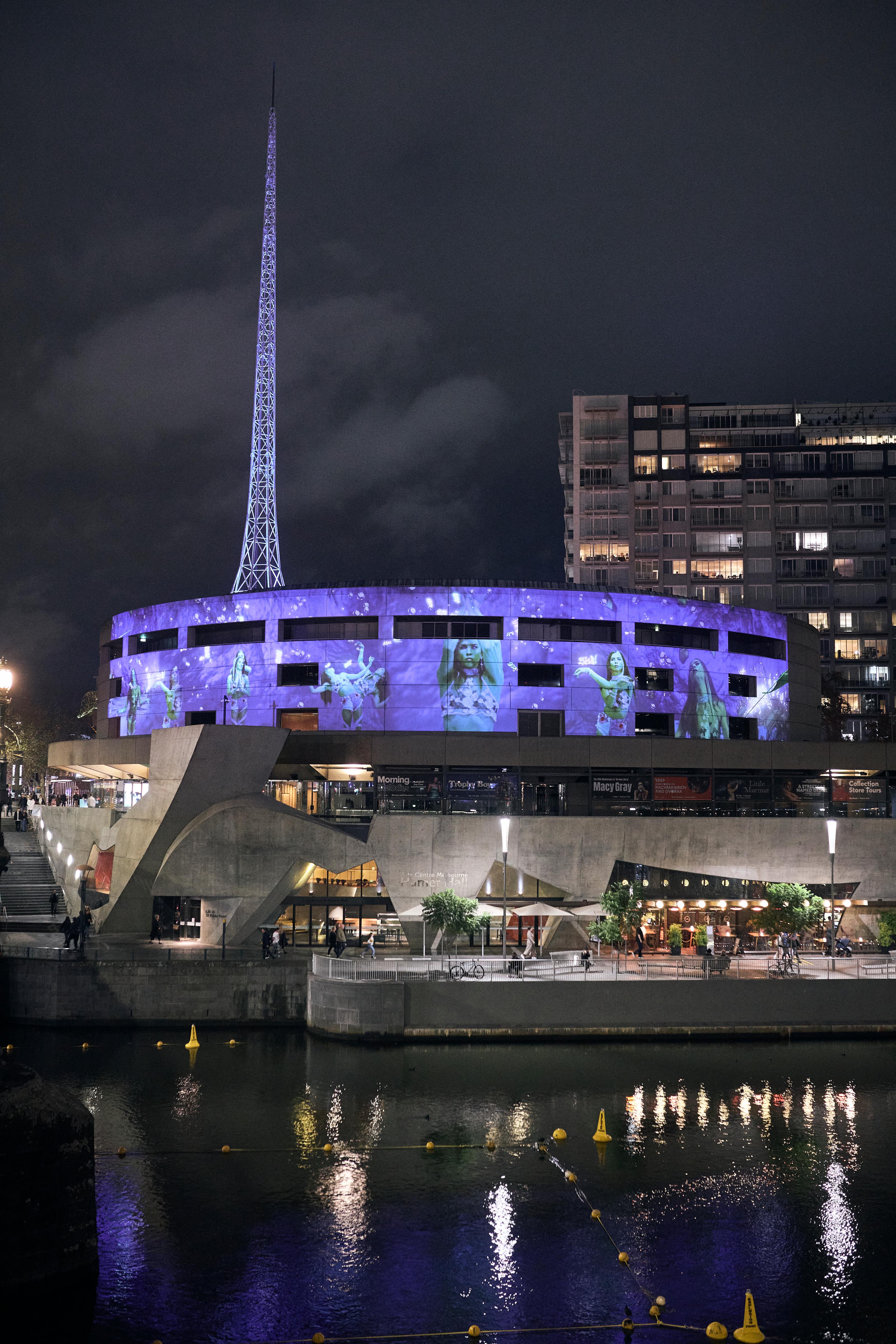 A nighttime view of Hamer Hall and Southbank with art projected onto Hamer Hall and a lit up city in the background.