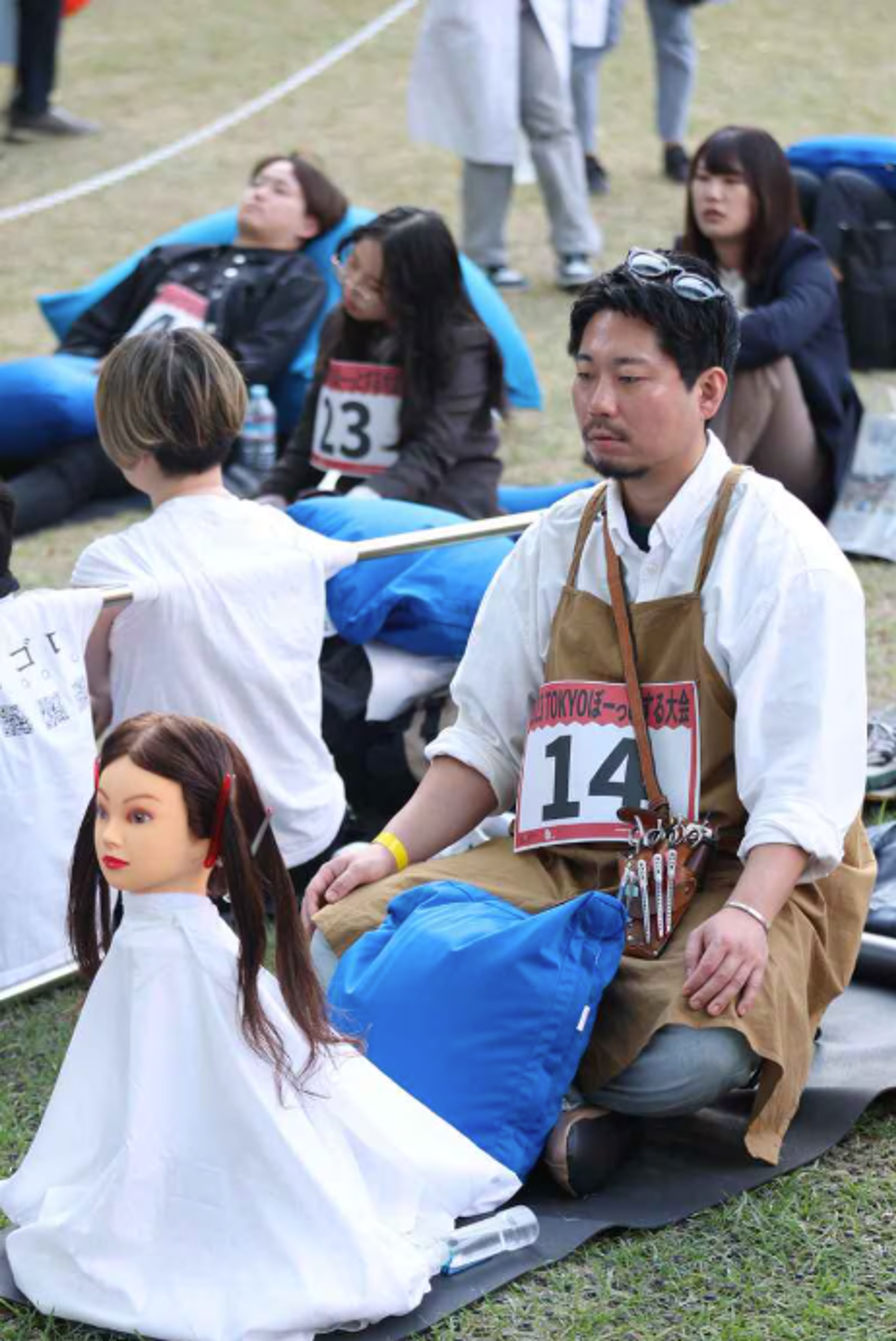An adult competitor sits legs crossed, with a doll's head dressed in white cloth in front of them