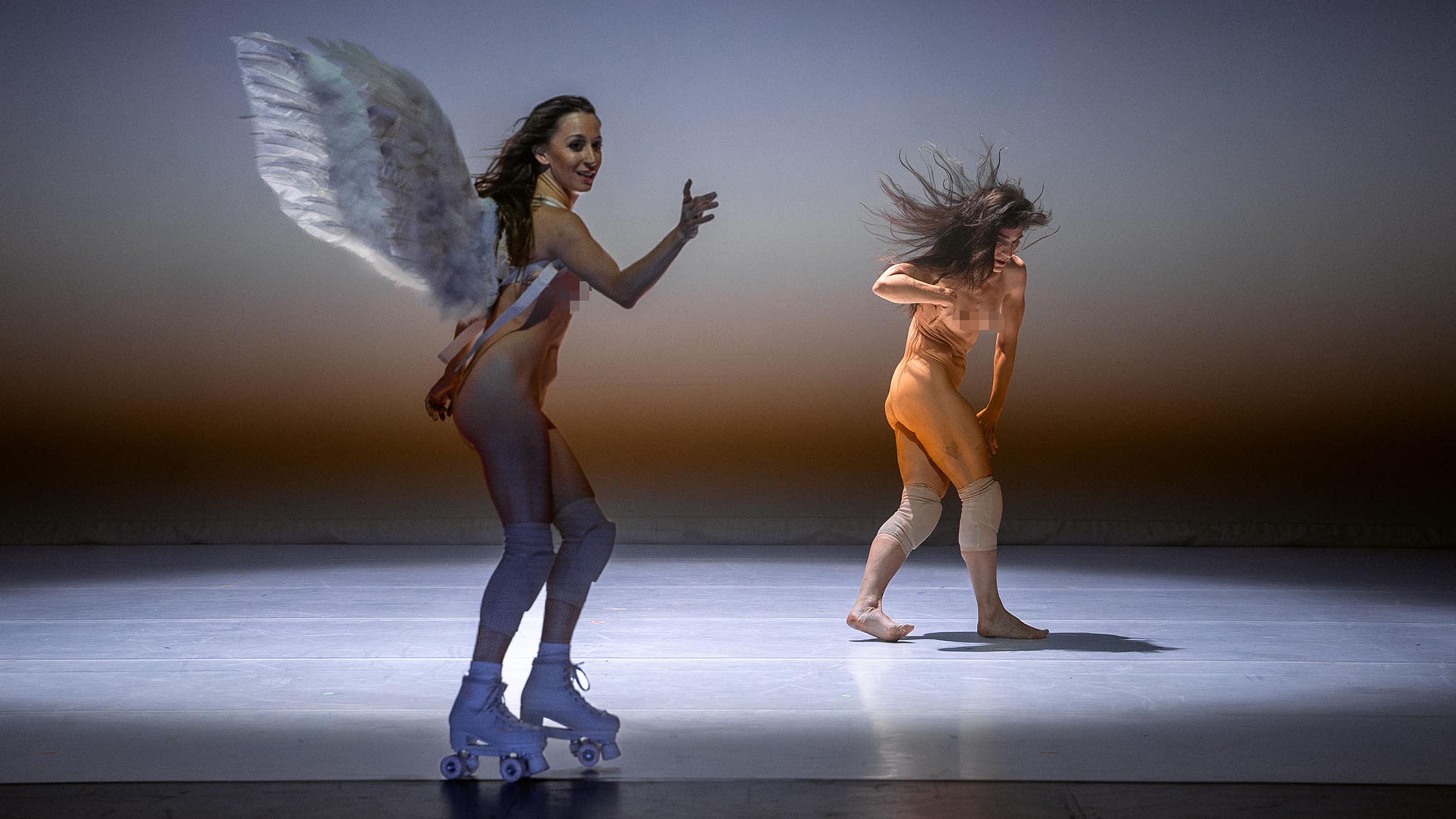 A person wearing fairy/angel wings and rollerblades in the foreground. A nude dancer wearing knee pads in the background.