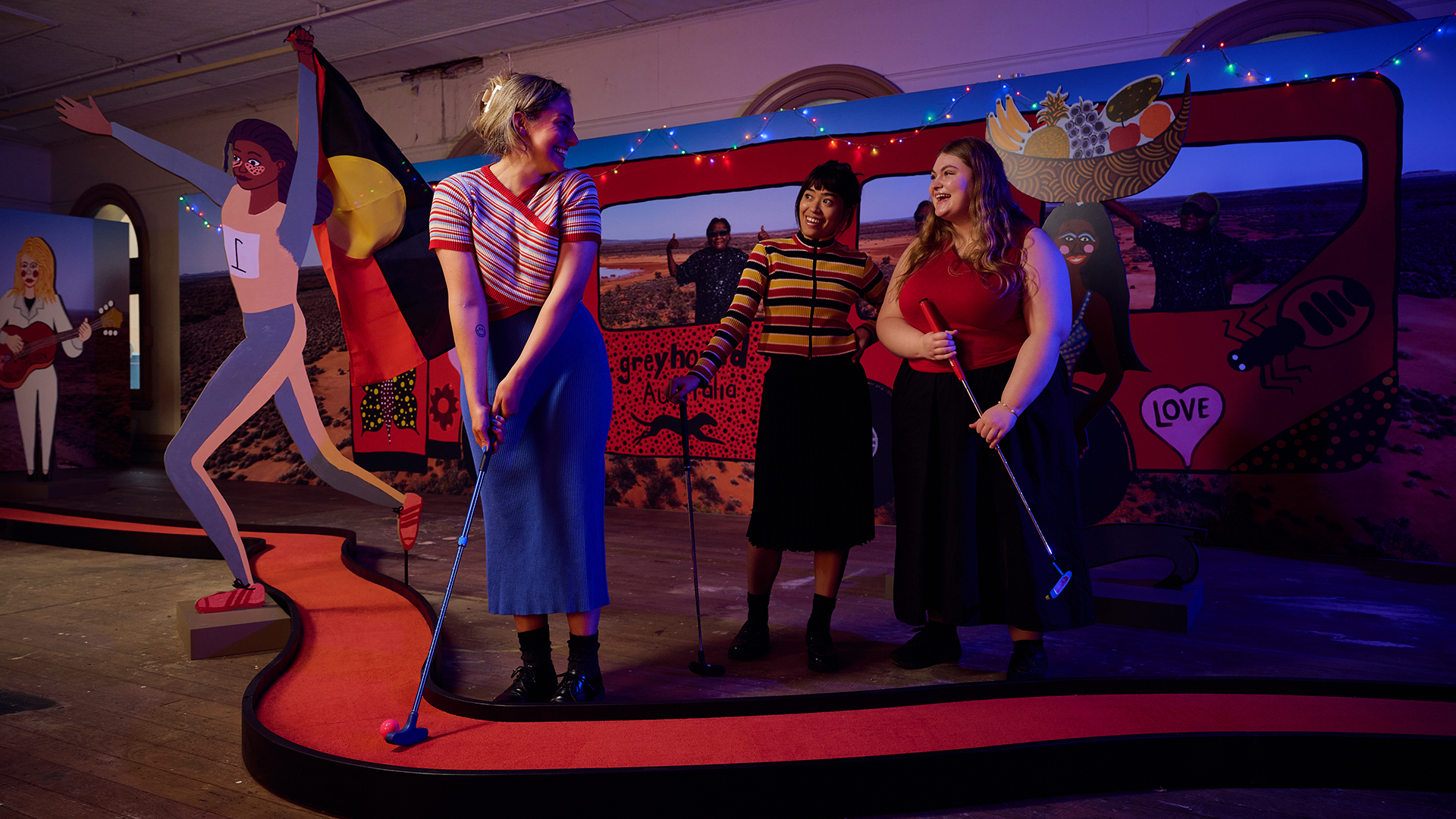 A woman plays mini golf with two friends, on the Kaylene Whiskey-designed hole.