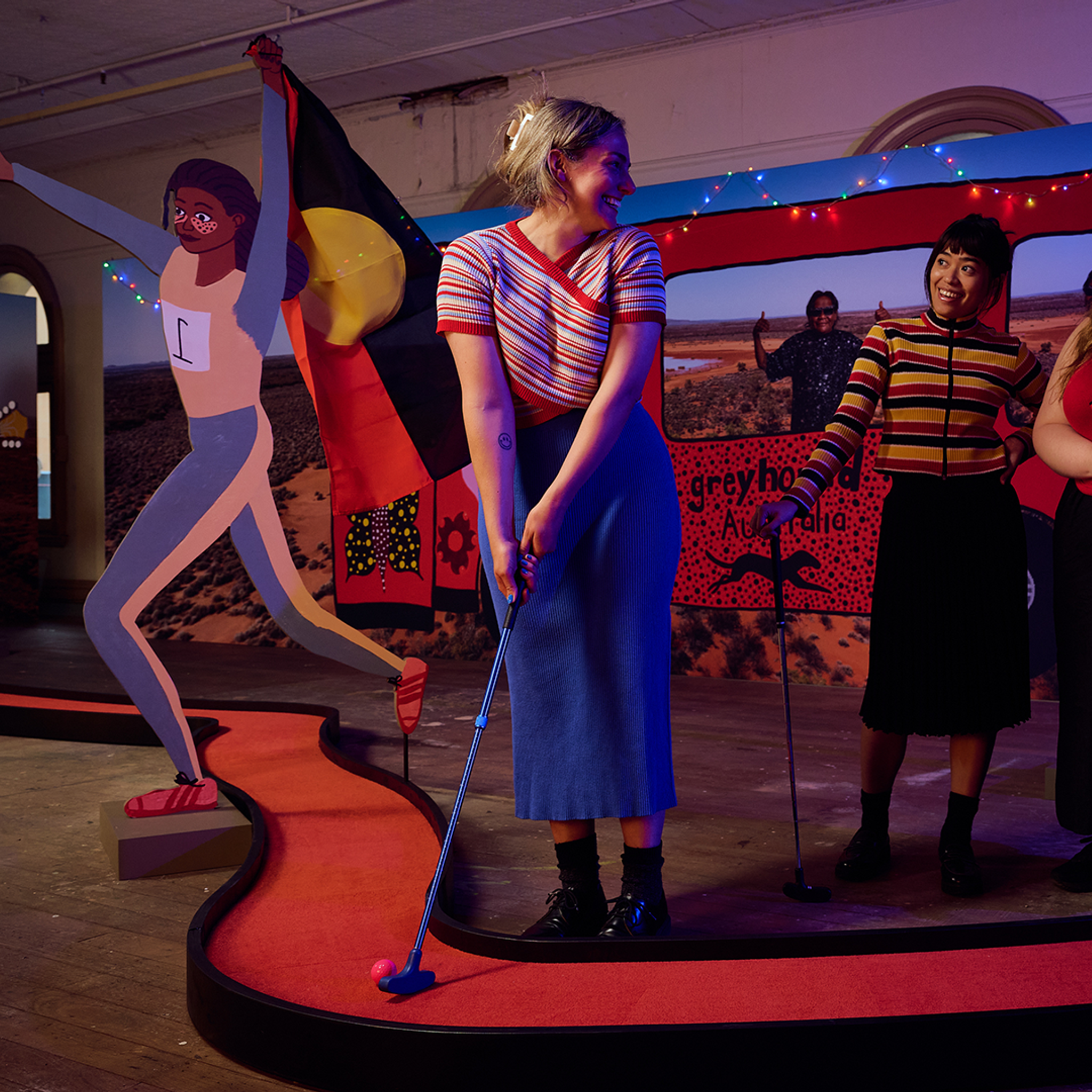 A woman plays mini golf with two friends, on the Kaylene Whiskey-designed hole.