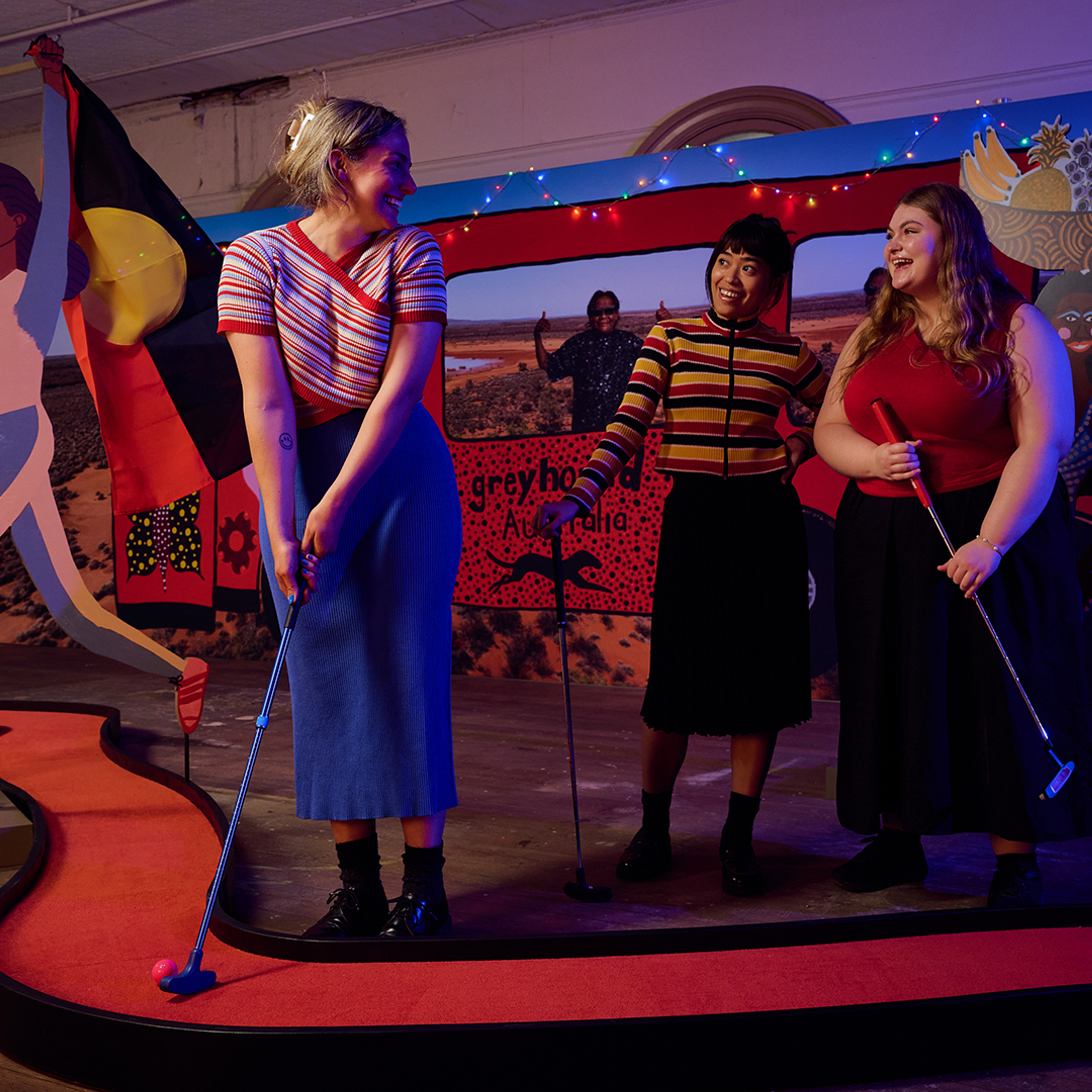 A woman plays mini golf with two friends, on the Kaylene Whiskey-designed hole.