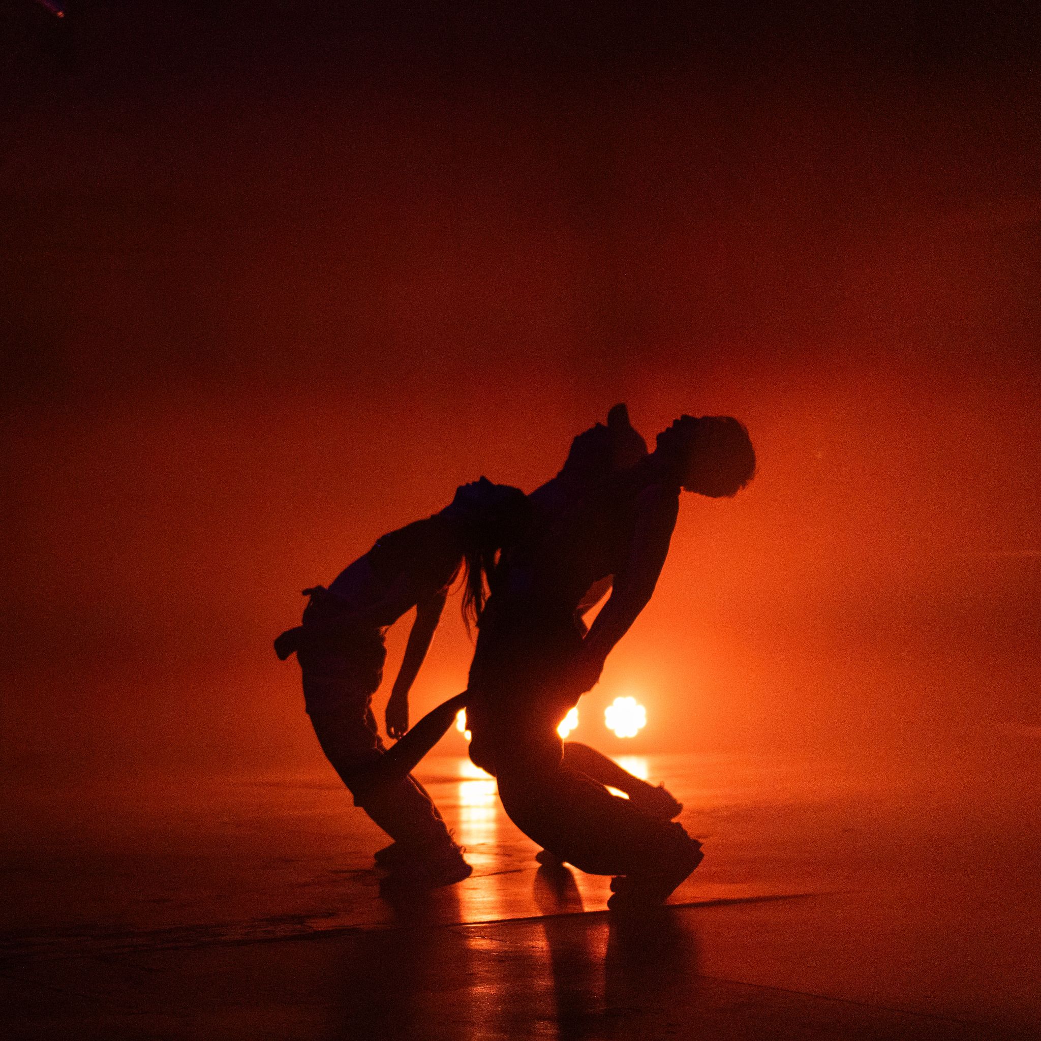 A silhouetted trio of dancers leaning backwards.