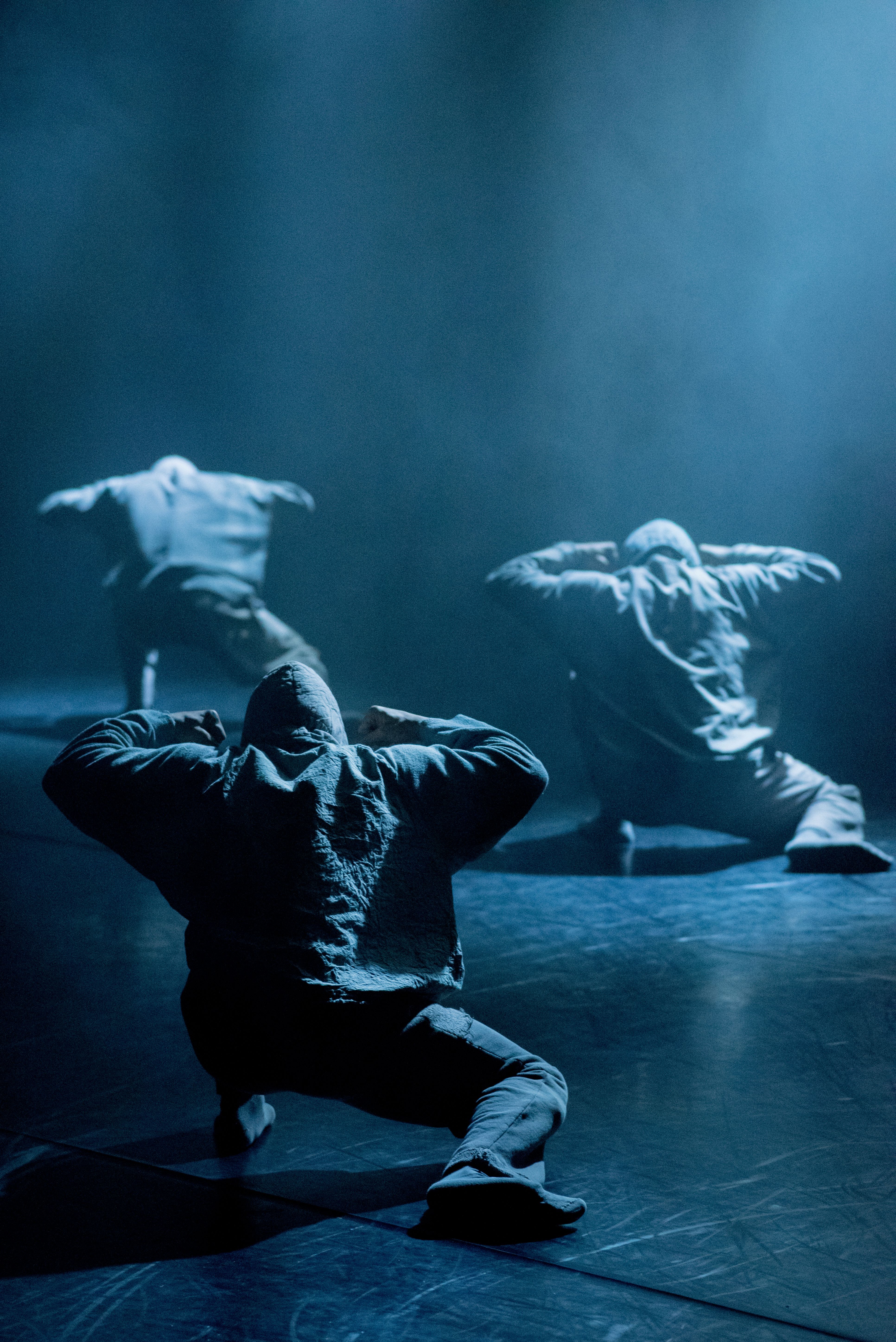 Three dancers in hoodies move away from the camera in a crouched position 