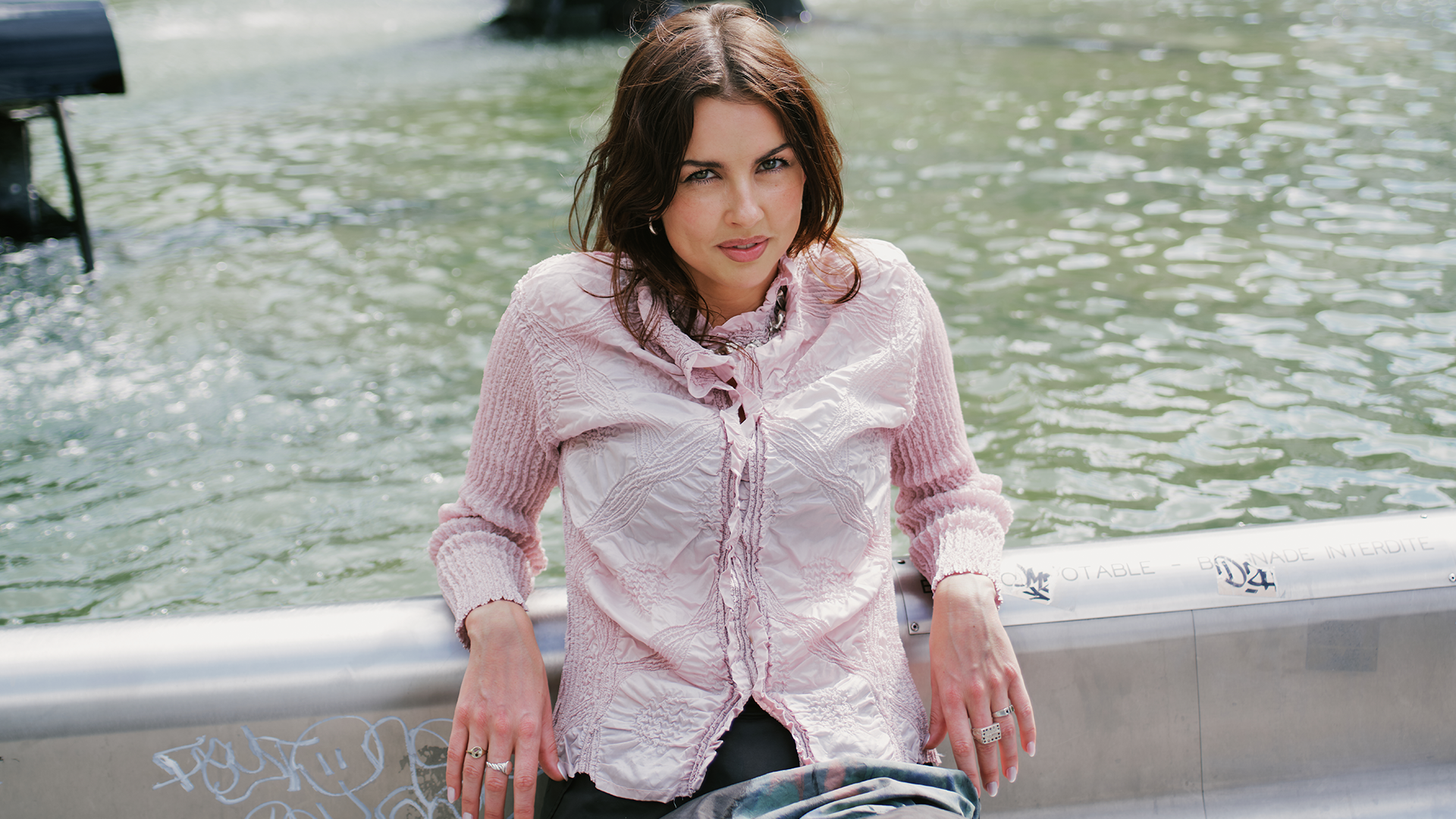Mikaela sits facing the camera, leaning her elbows on a fountain behind her