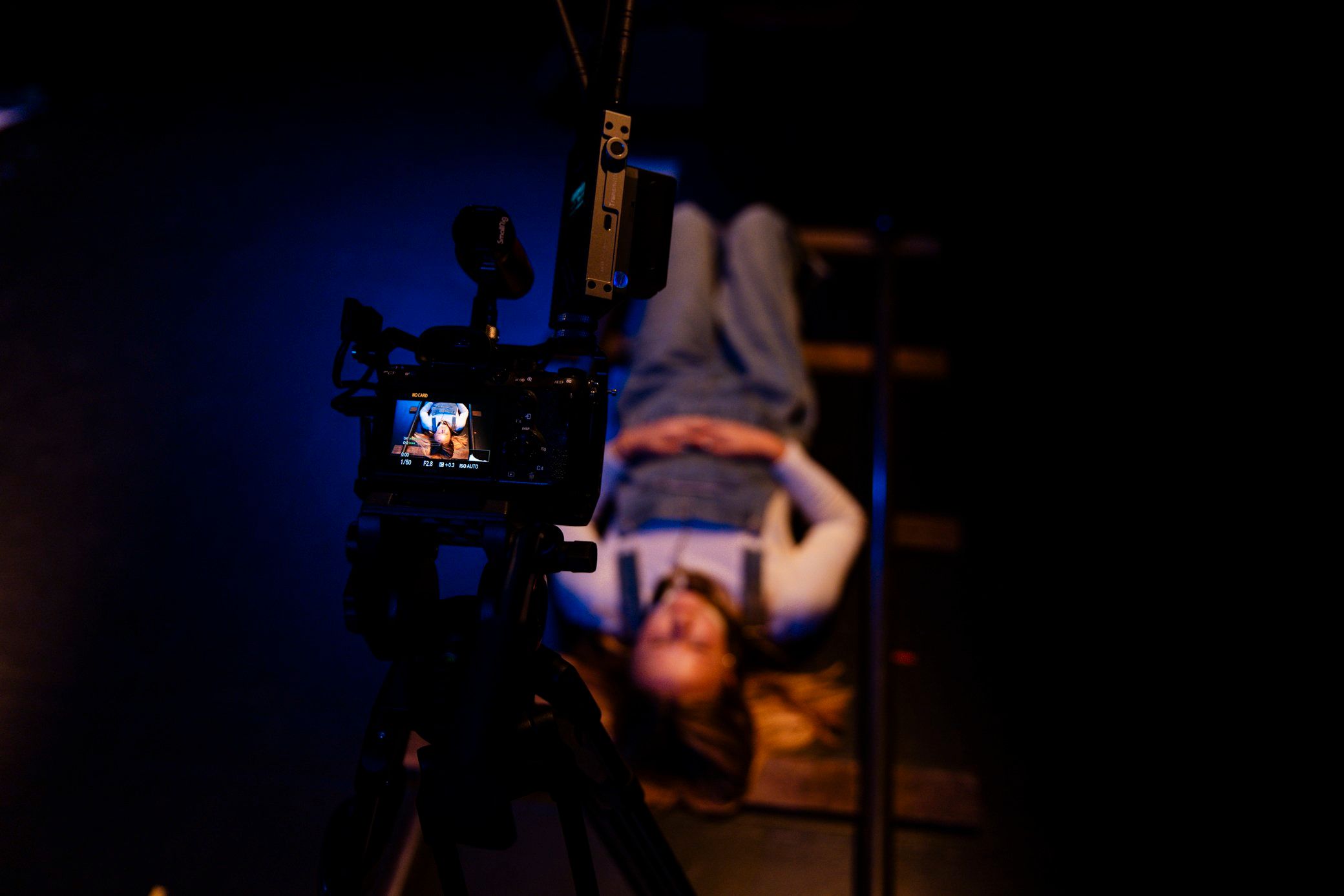 A young person hangs upside down like they’re on monkey bars. They are filming themselves with a camera 