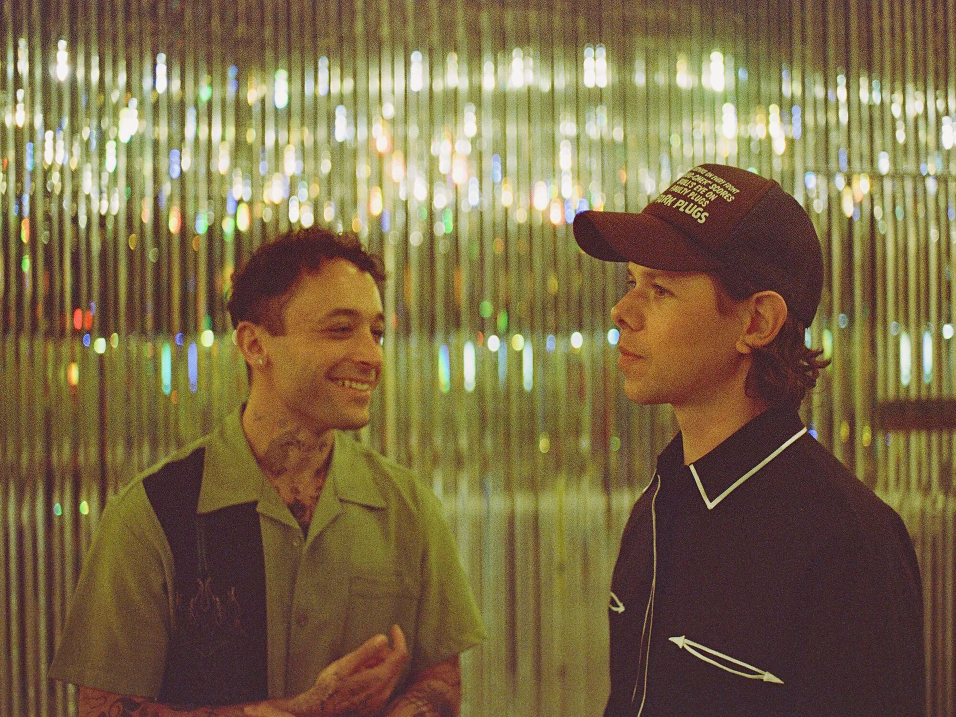 One person on the left is smiling, while the person on the right is wearing a hat and posing sideways.