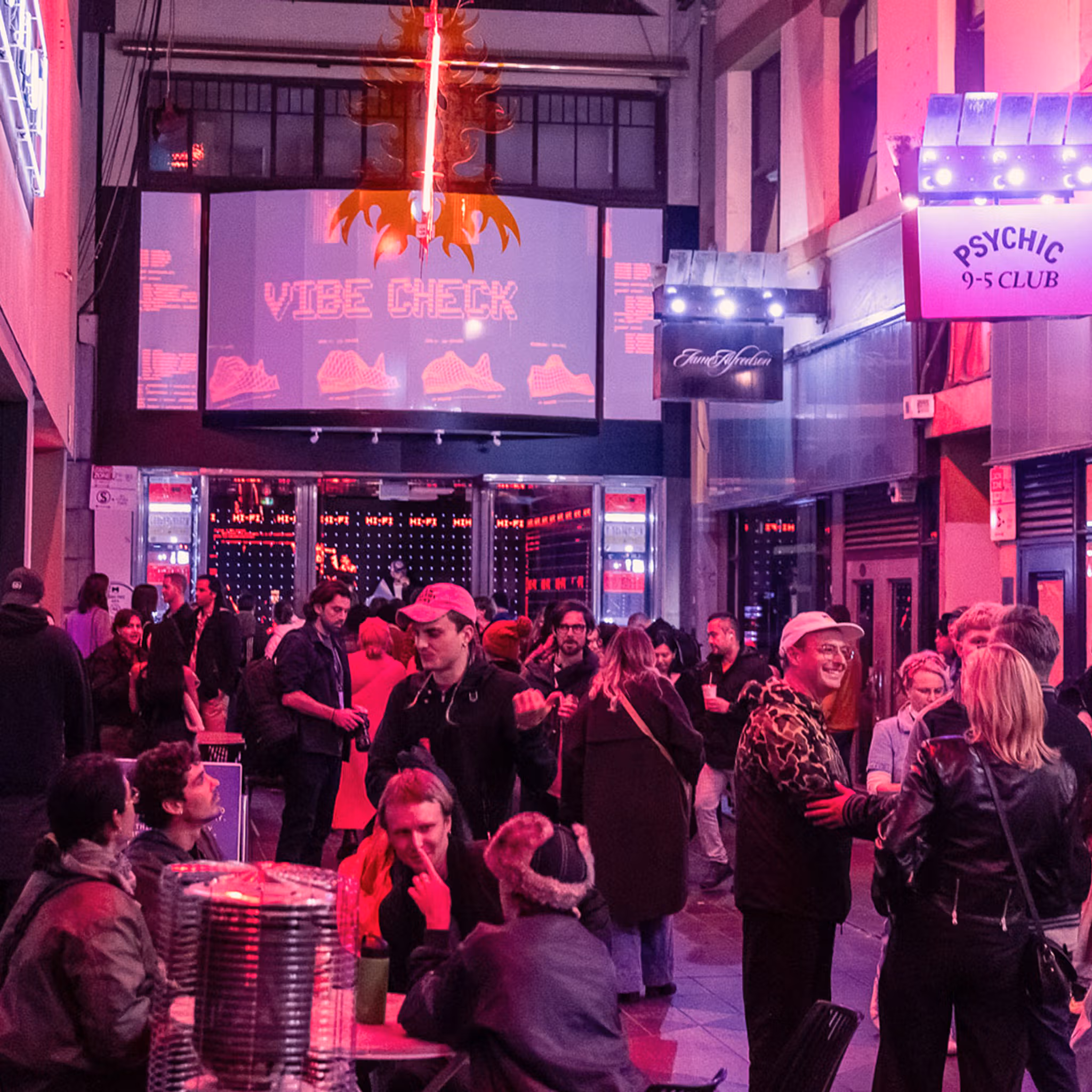A wide view of a busy arcade at night. People are enjoying drinks and listening to a DJ