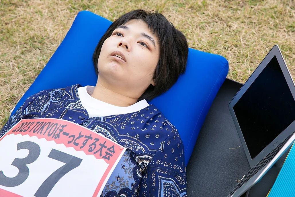 A young person lies on a blue pillow and mat. Staring blankly upwards, with a small lcd screen beside her 