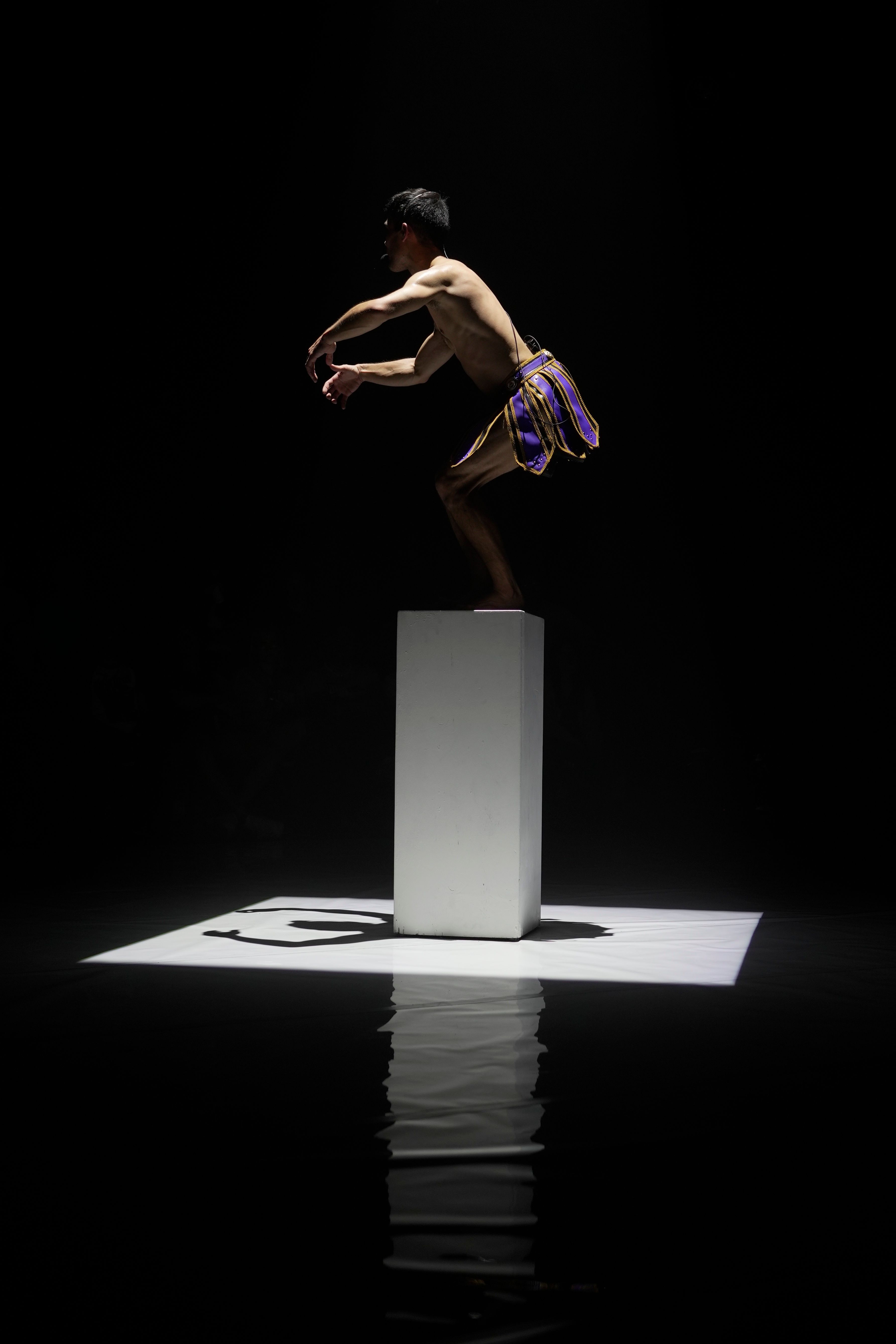A performer in a skirt poses on top of the podium as a square spotlight is cast down upon them.  