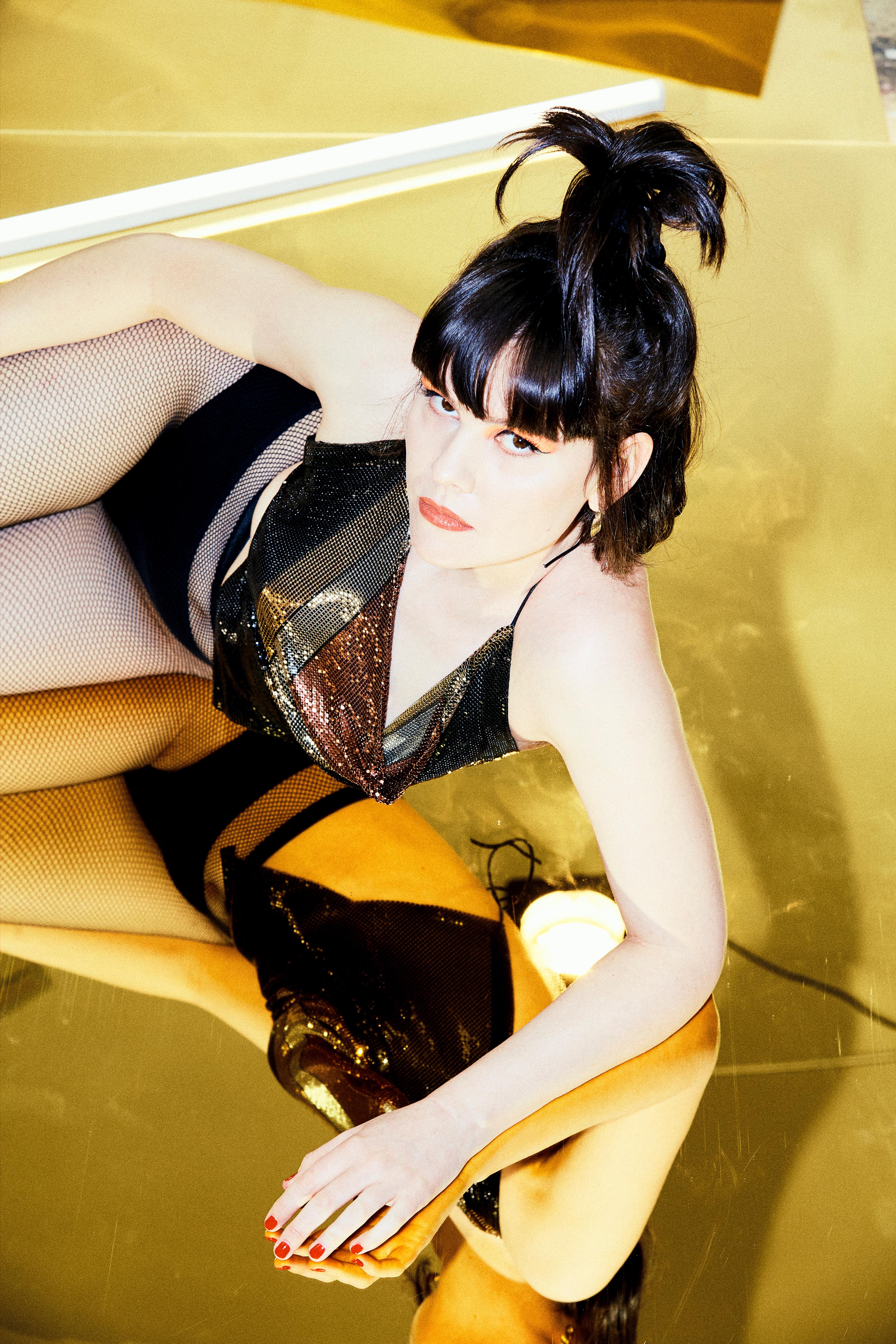 Lying on a mirrored floor Ela Stiles (dark bob, white woman) looks into the camera