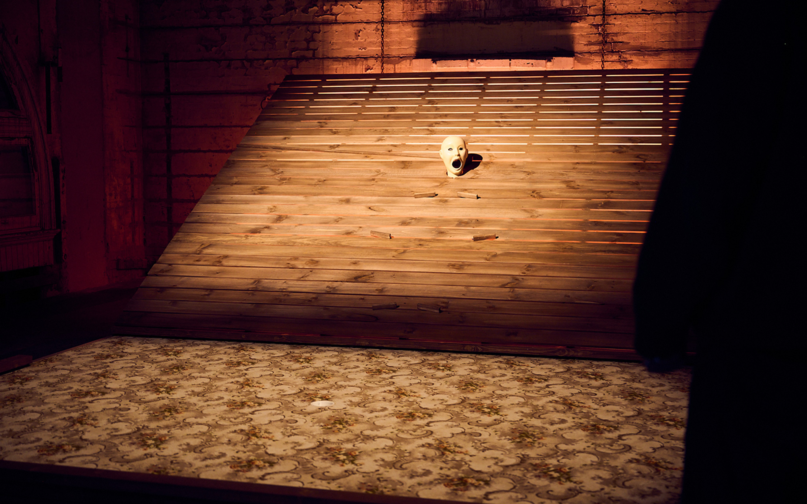 A menacing carnival-style rotating clown head with open mouth pops out of the centre of a wooden staircase