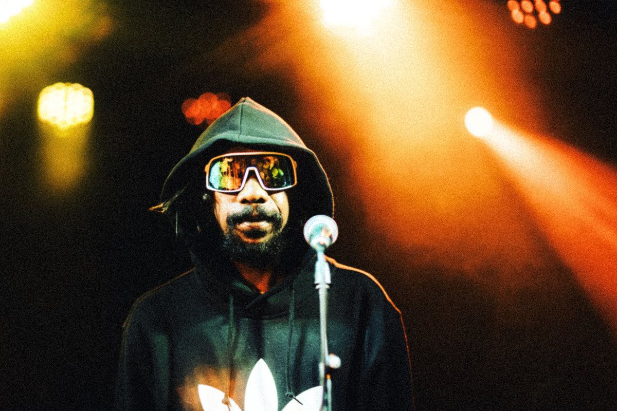 Keanu Nelson stands in front of a mic in a hoodie and large sunglasses