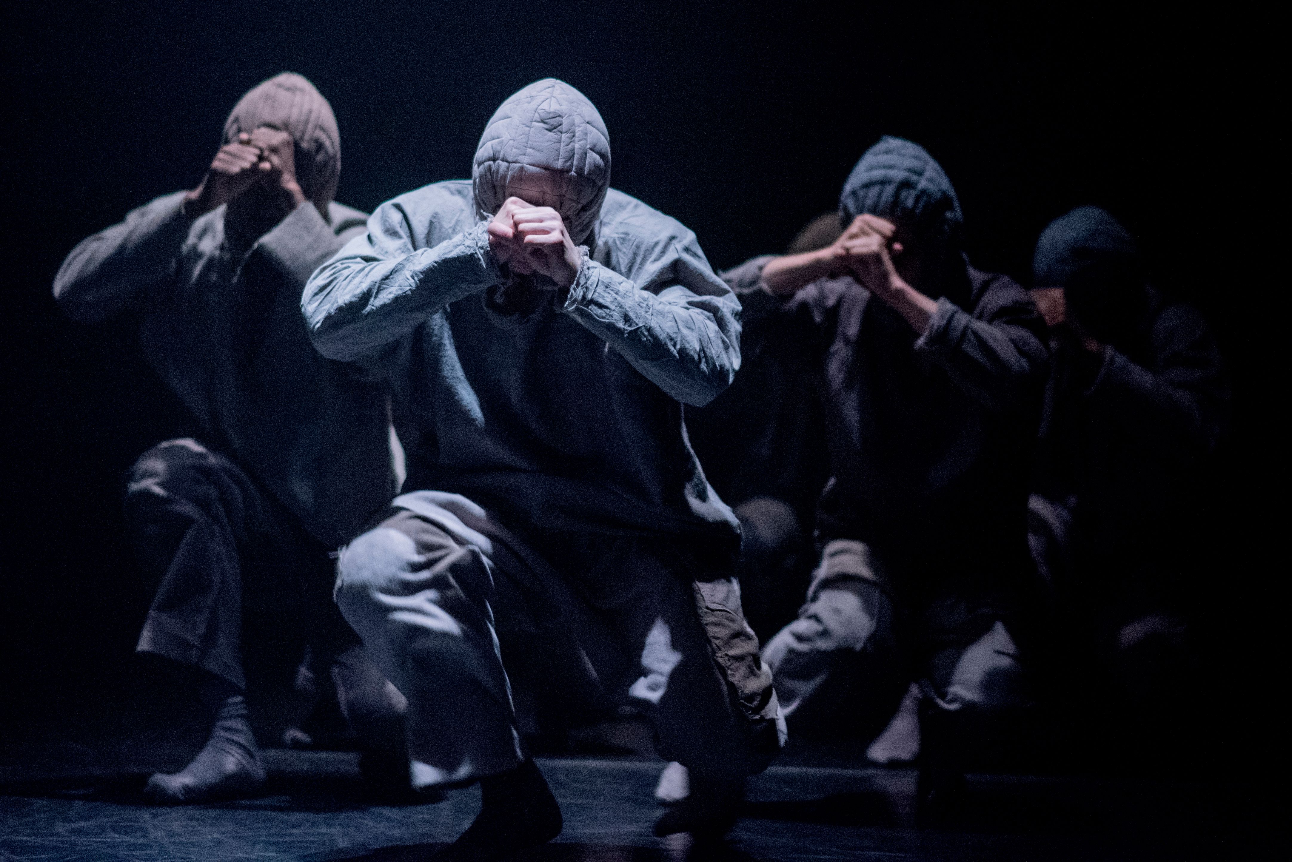  Four dancers in hoodies move towards the camera in a crouched position 