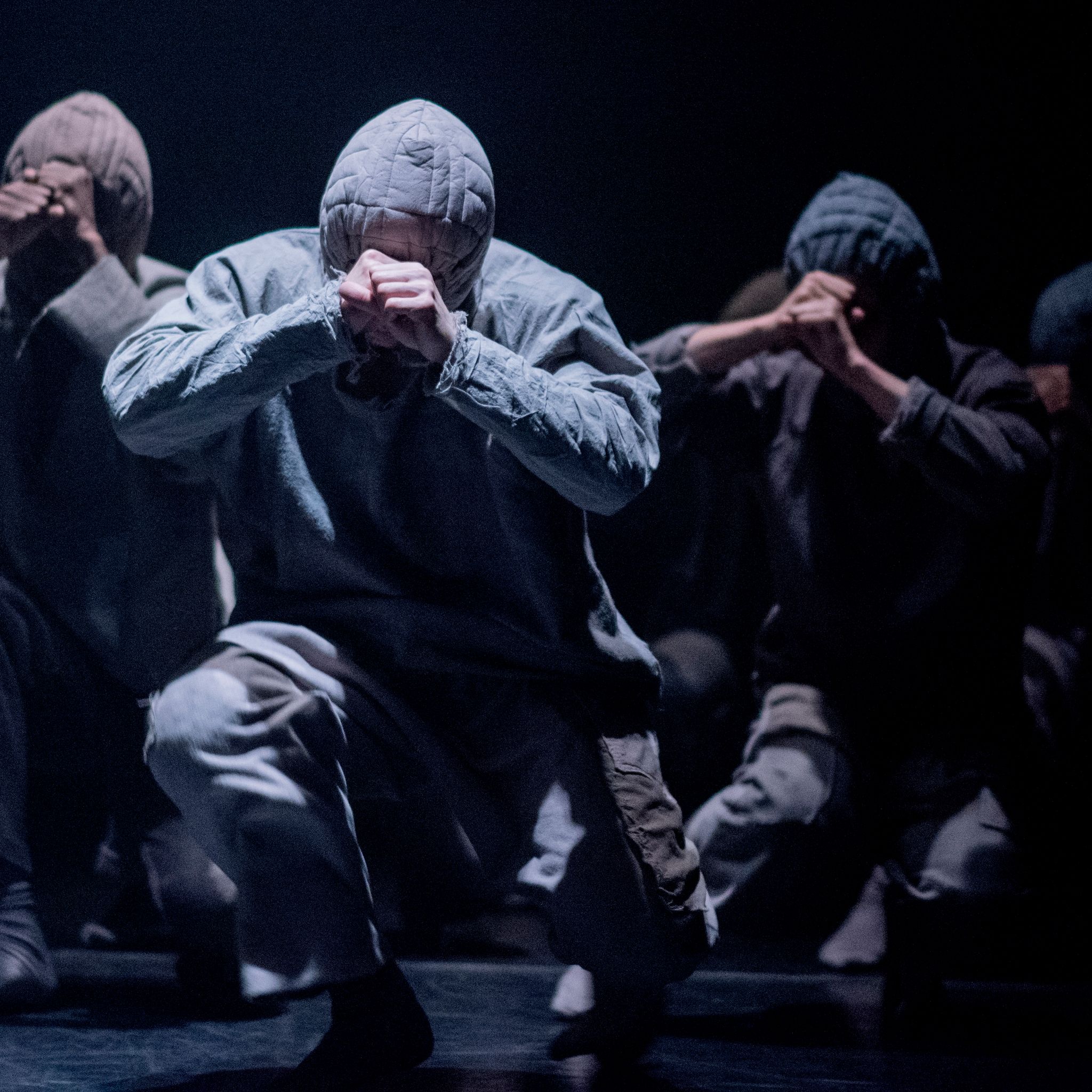 Four dancers in hoodies move towards the camera in a crouched position