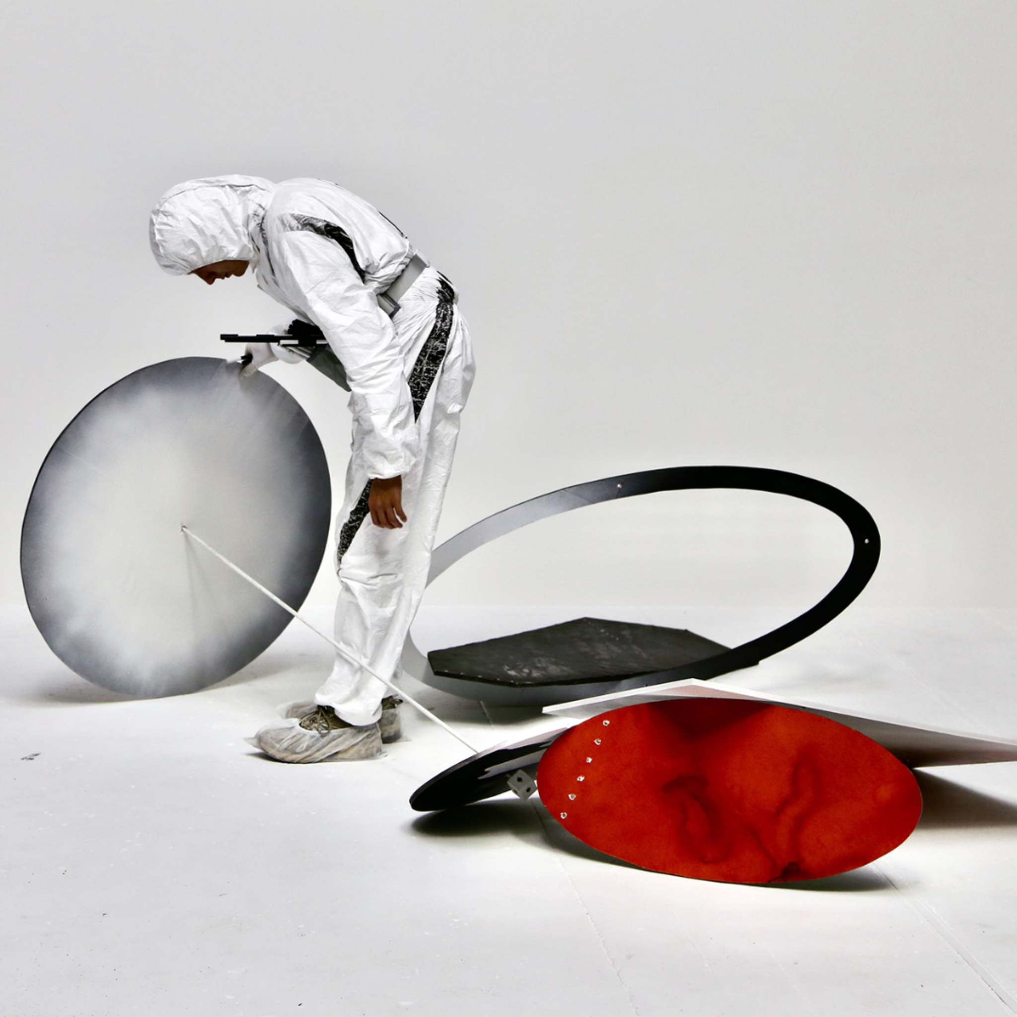 A person in a hazmat suit rolls a large circular disc on its side.