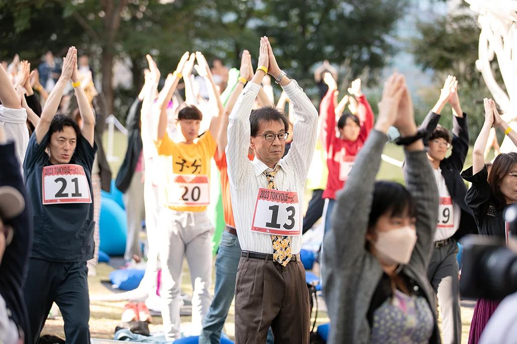 Competitors in the Space Out Competition dress in various outfits with numbers on their fronts, standing with their arms extended upward and palms facing each other 