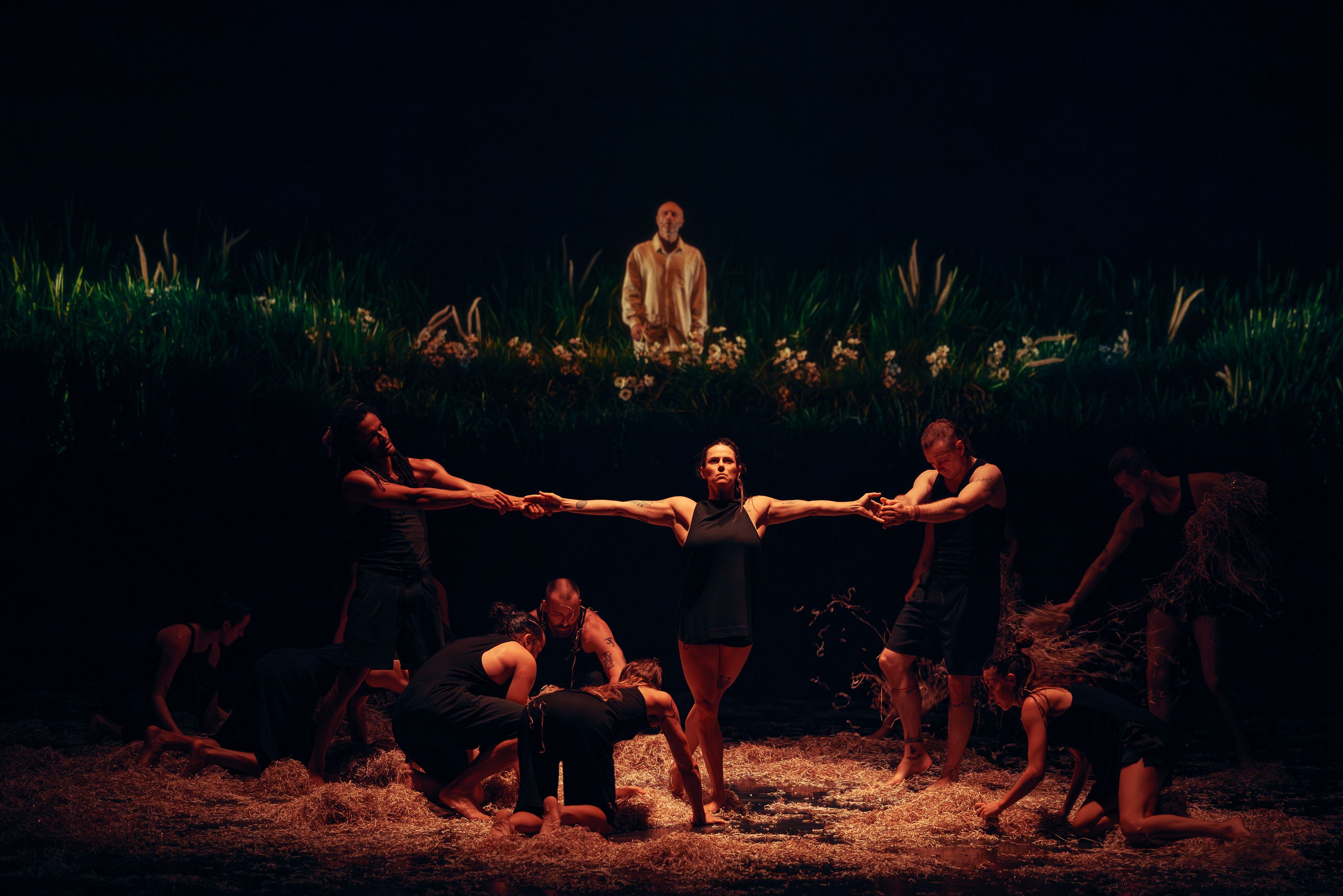 Person in the centre has arms outstretched, being pulled by two others on either side. Several other people bow down before them in a circle formation. 