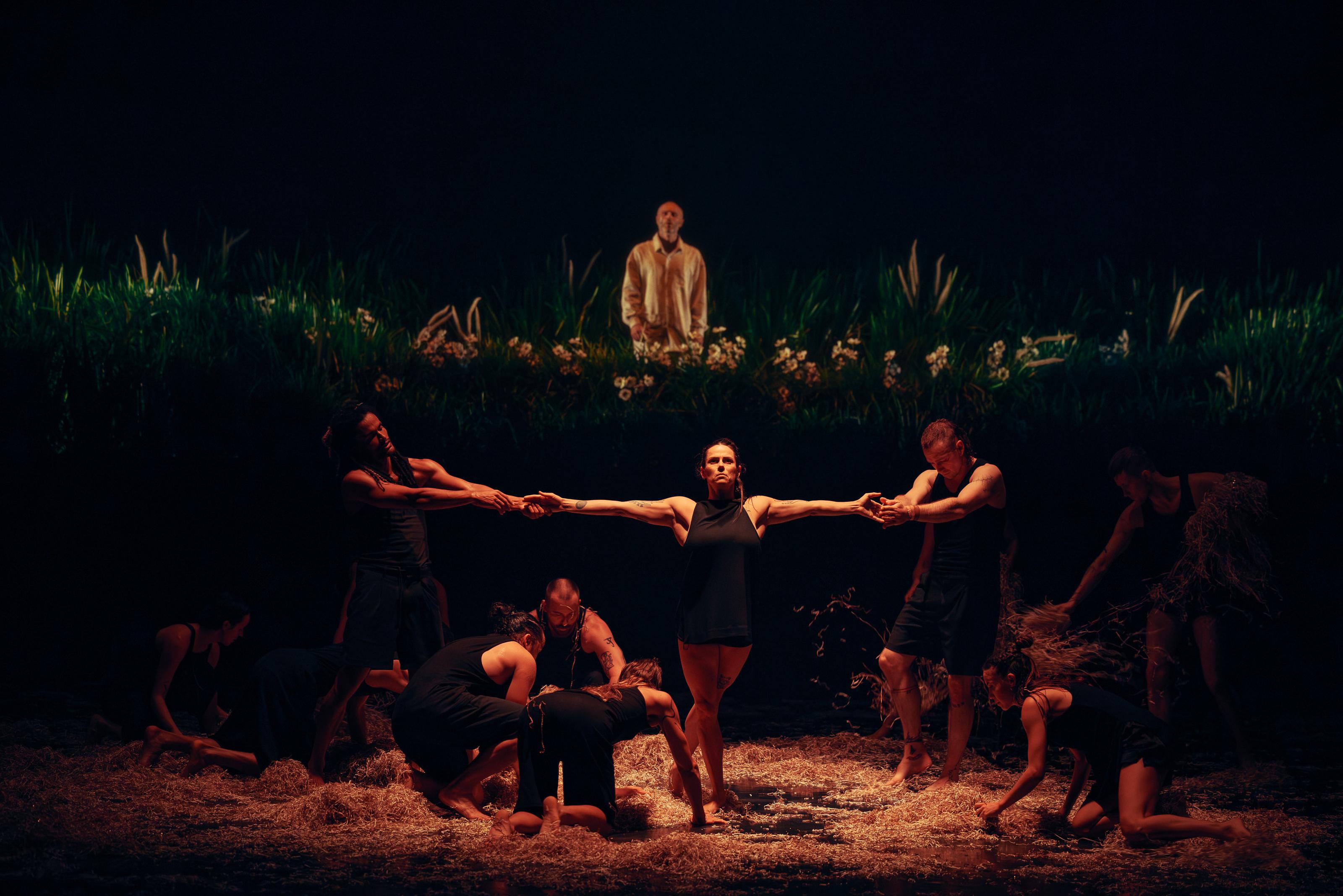 Person in the centre has arms outstretched, being pulled by two others on either side. Several other people bow down before them in a circle formation.